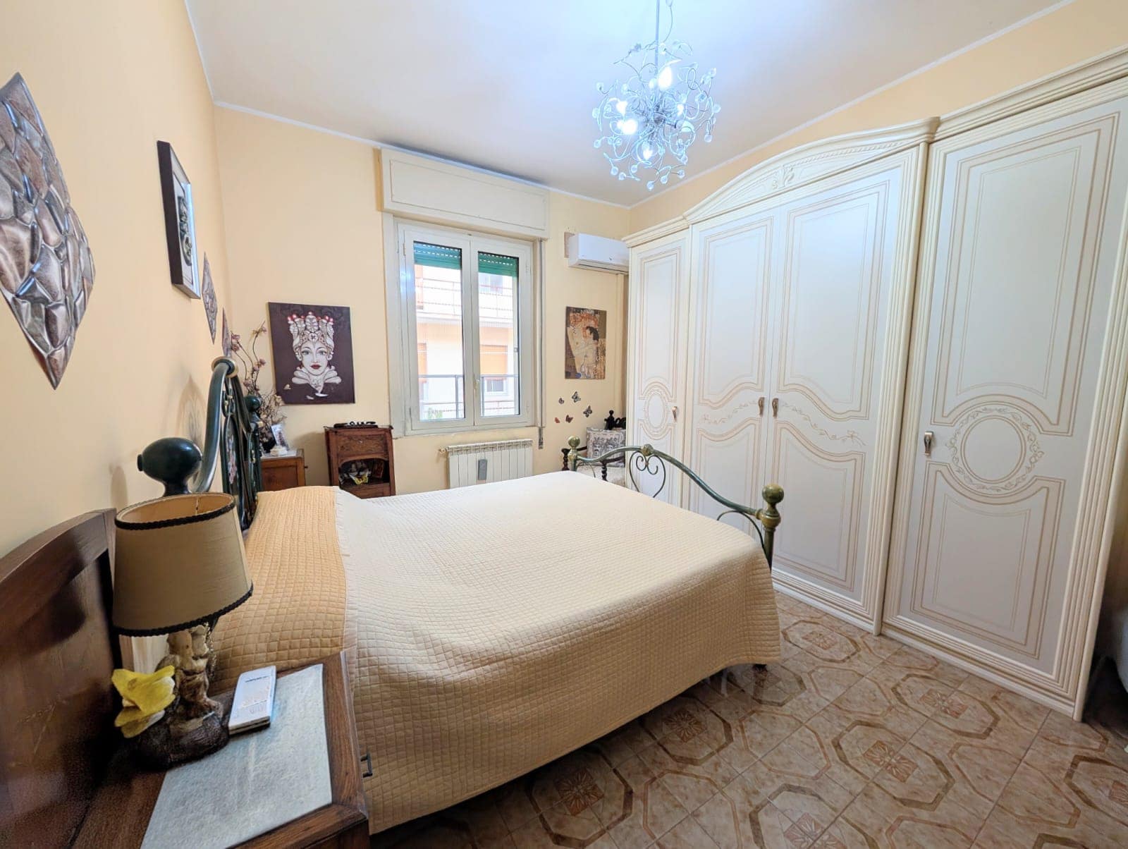Una camera da letto spaziosa con armadio a muro bianco, letto matrimoniale, lampada da tavolo e decorazioni alle pareti, illuminata da luce naturale attraverso una finestra.