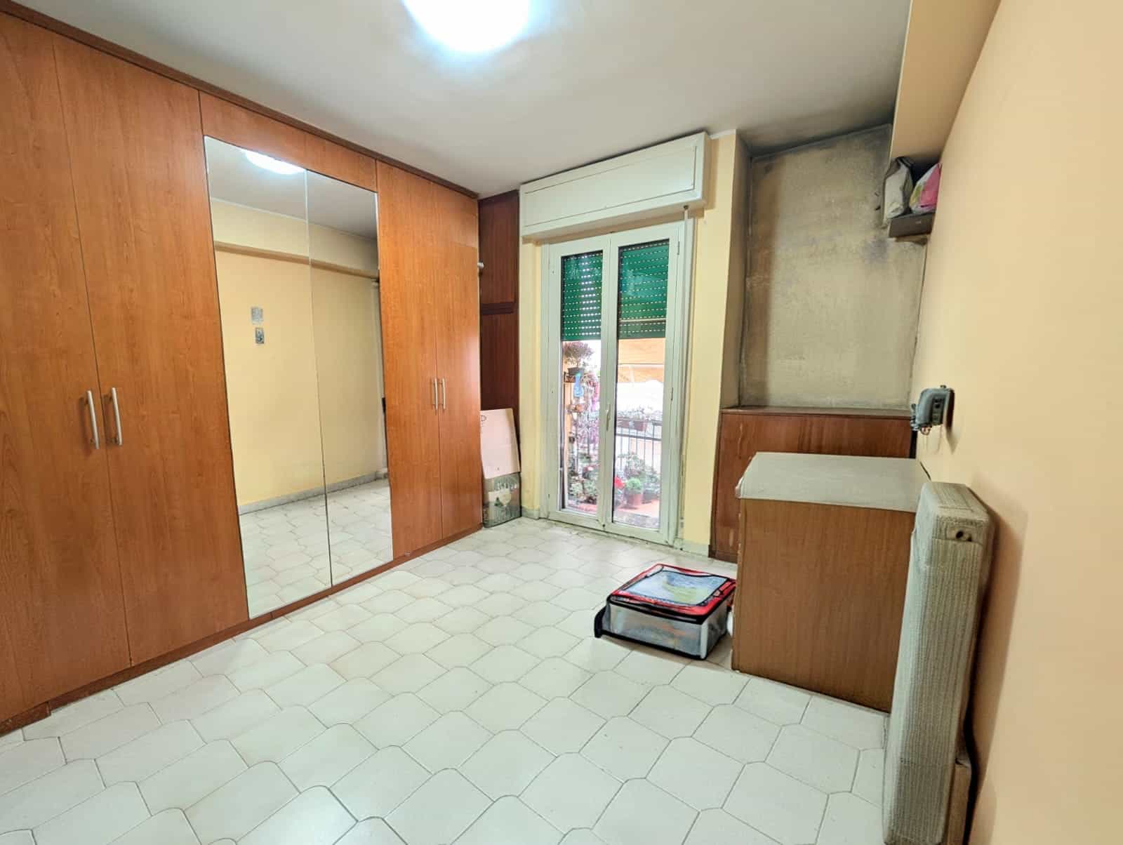 Armadio a muro con ante a specchio e porta finestra con balcone, stanza luminosa e funzionale.