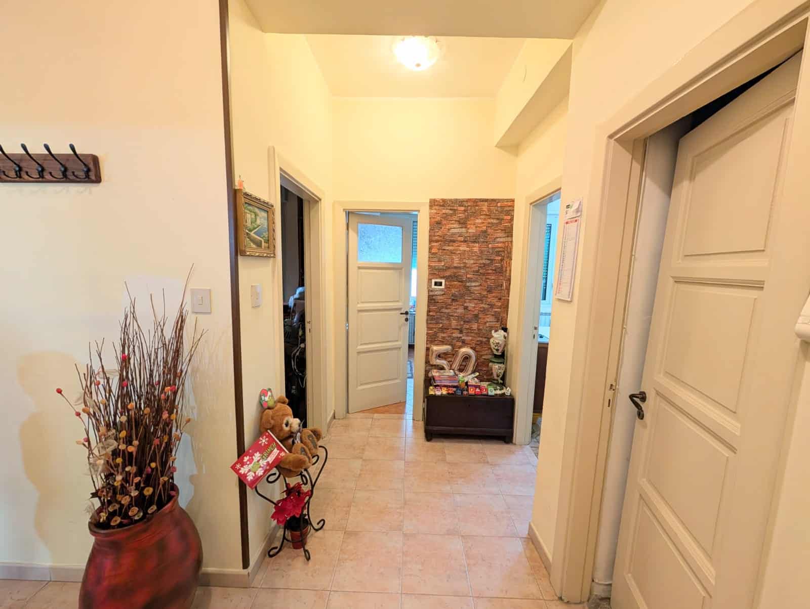 Porte d'ingresso e corridoio di casa con decorazioni natalizie, pareti bianche e pavimento in piastrelle beige, ambiente accogliente e ben illuminato.