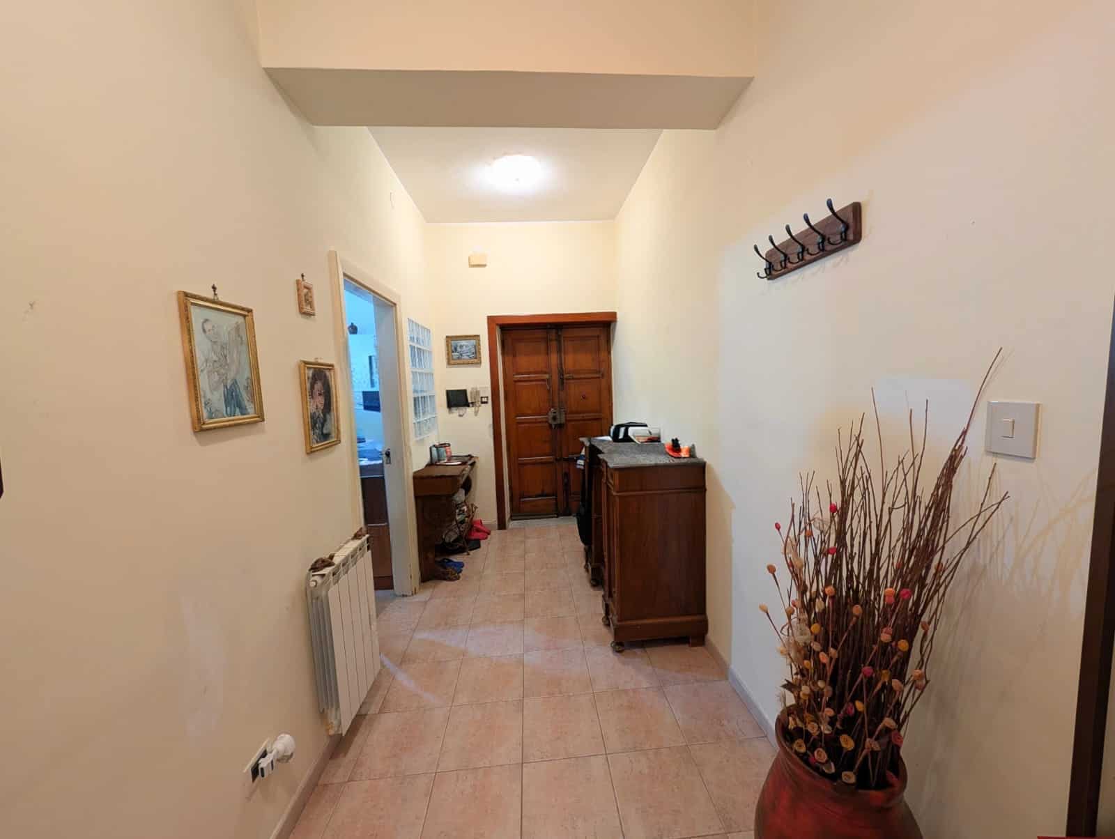 Porte d'ingresso in legno naturale in un ingresso di casa con pareti chiare, decorazioni e un vaso con rami secchi, ambiente accogliente e ben illuminato.