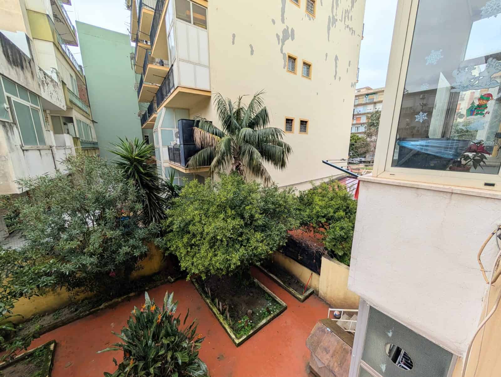 Verde condominiale con piante e alberi, vista su cortile interno di un edificio residenziale, con balconi e finestre, in un contesto urbano, ambiente tranquillo e naturale.
