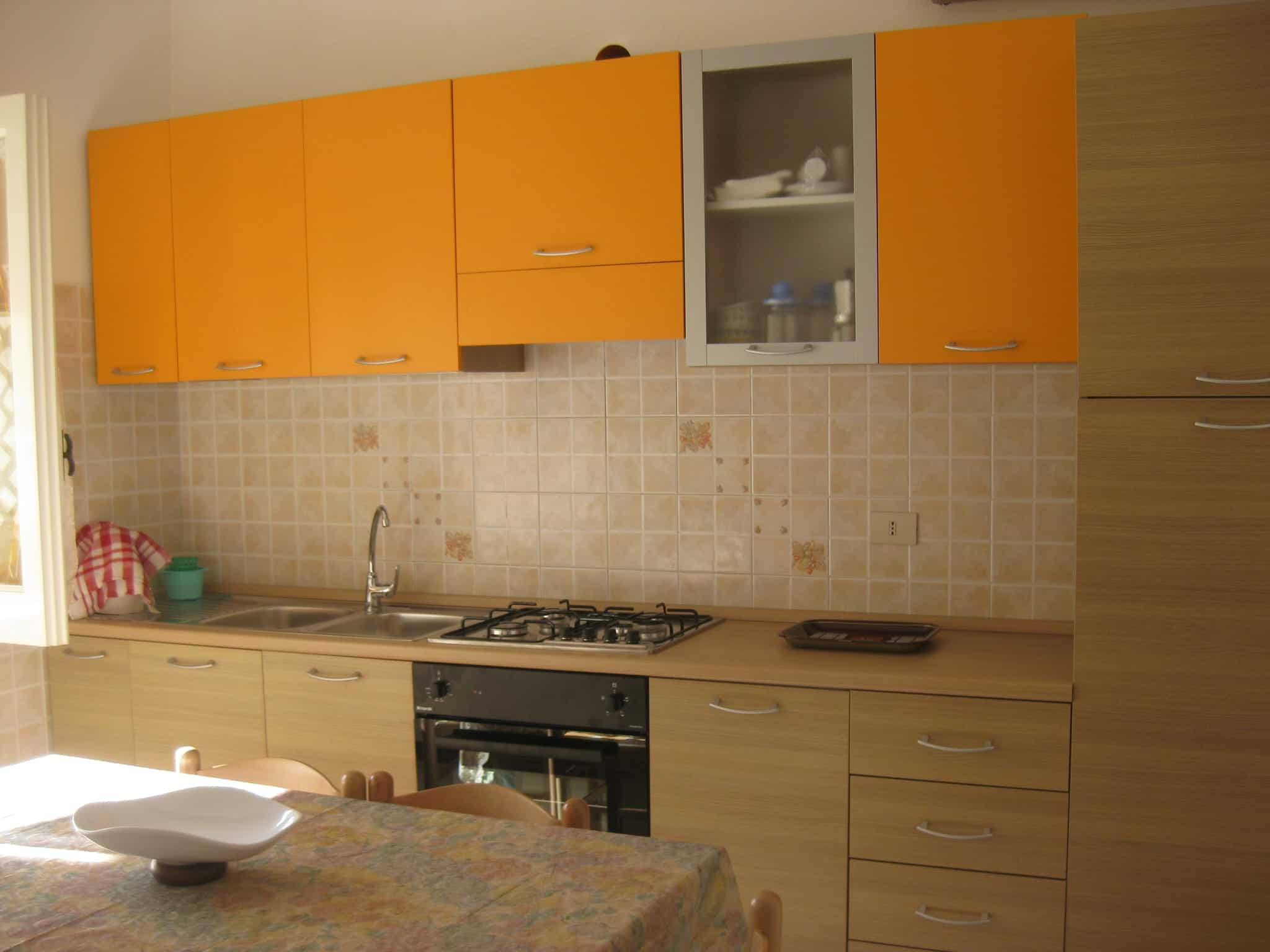 Piano cucina moderno con ante arancioni e dettagli in vetro, ideale per ambienti abitativi funzionali e di design. Cucina compatta con piano di lavoro spazioso, forno e zona cottura, perfetta per cuci.