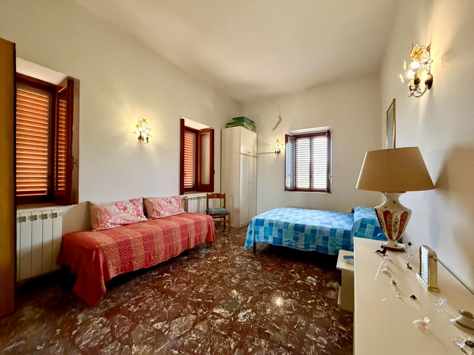 Ampia camera da letto con due finestre, arredi classici e pavimento in marmo, ideale per soggiorni confortevoli e rilassanti.
