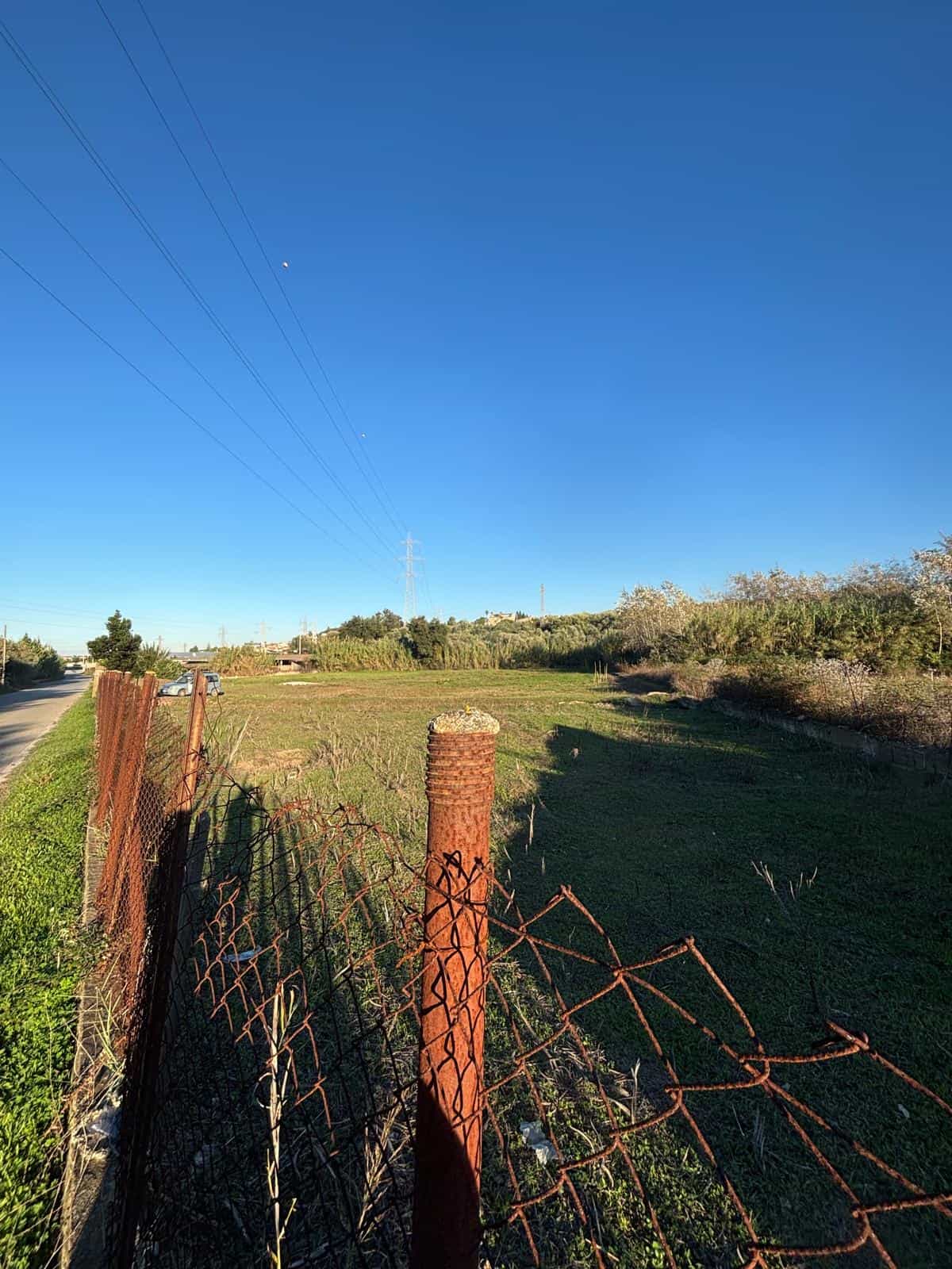 Barriera di recinzione rustica in ferro arrugginito con campagna verde e cielo azzurro, zona rurale tranquilla, ideale per proprietà immobiliari NextCasa in Italia.