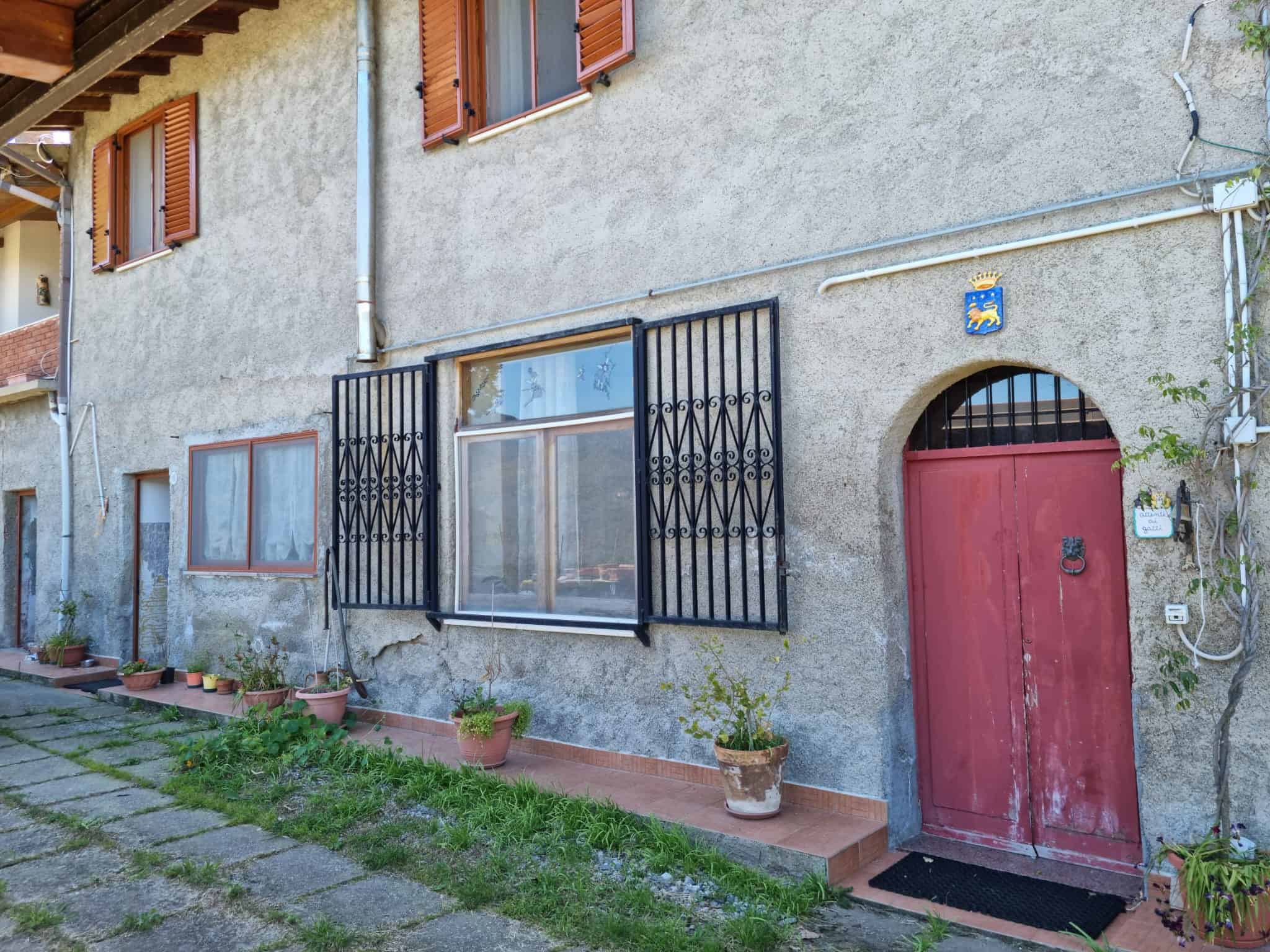 Vetro e persiane in legno sulla facciata di una casa tradizionale italiana con piante in vaso lungo il muro esterno.