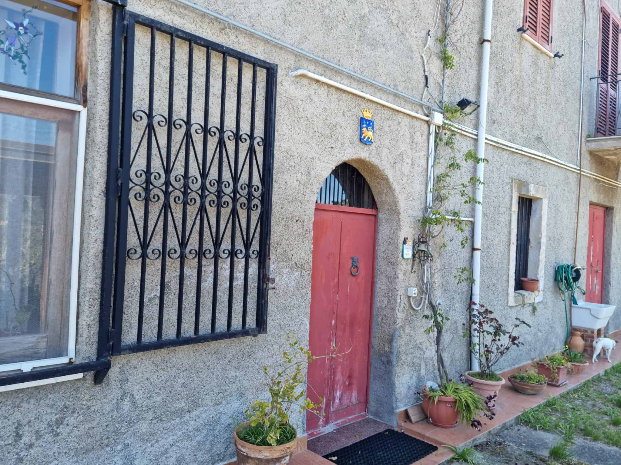 Porta d'ingresso in legno rosso con arco, decorata con piante in vaso e recinzione in ferro battuto, facciata di un edificio storico in pietra, atmosfera accogliente e autentica.