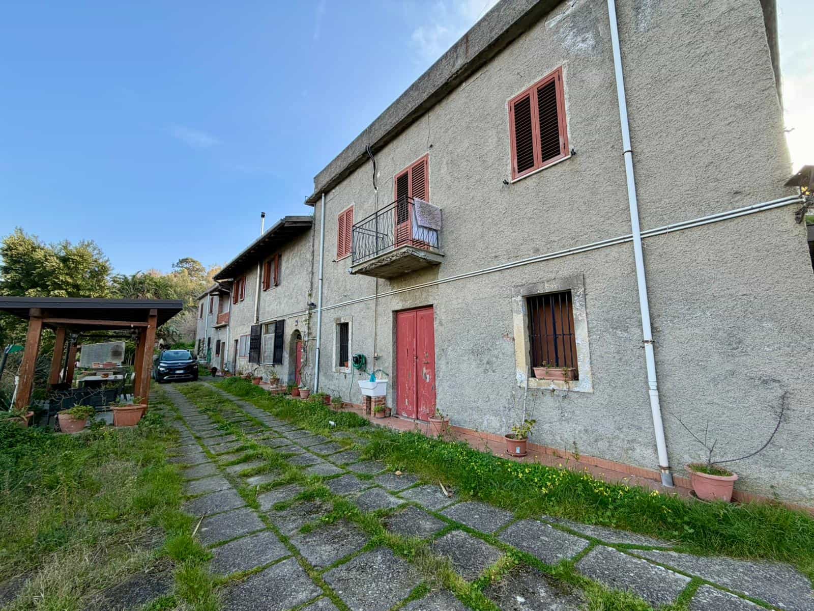 Edificio residenziale in stile rustico con finestre e balcone, situato in un'area verde, ideale per investimenti immobiliari o ristrutturazioni in Italia.