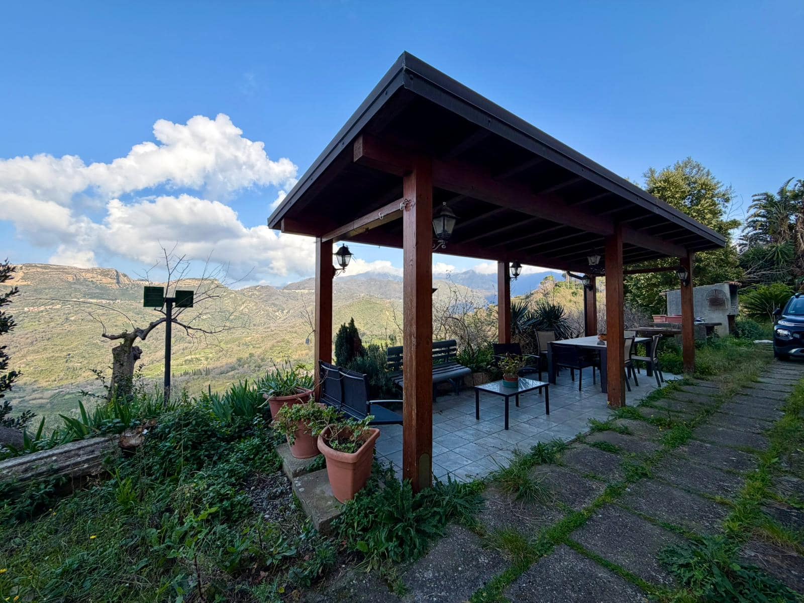 Riparo esterno in legno con vista panoramica sulle colline e il cielo azzurro, ideale per relax e convivialità all'aperto.