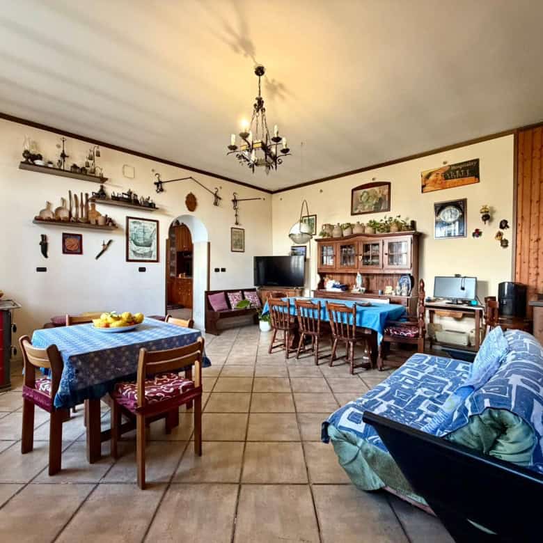 Interno di una casa accogliente con mobili in stile rustico, tavolo da pranzo, divano e decorazioni vintage, ambiente luminoso e spazioso.