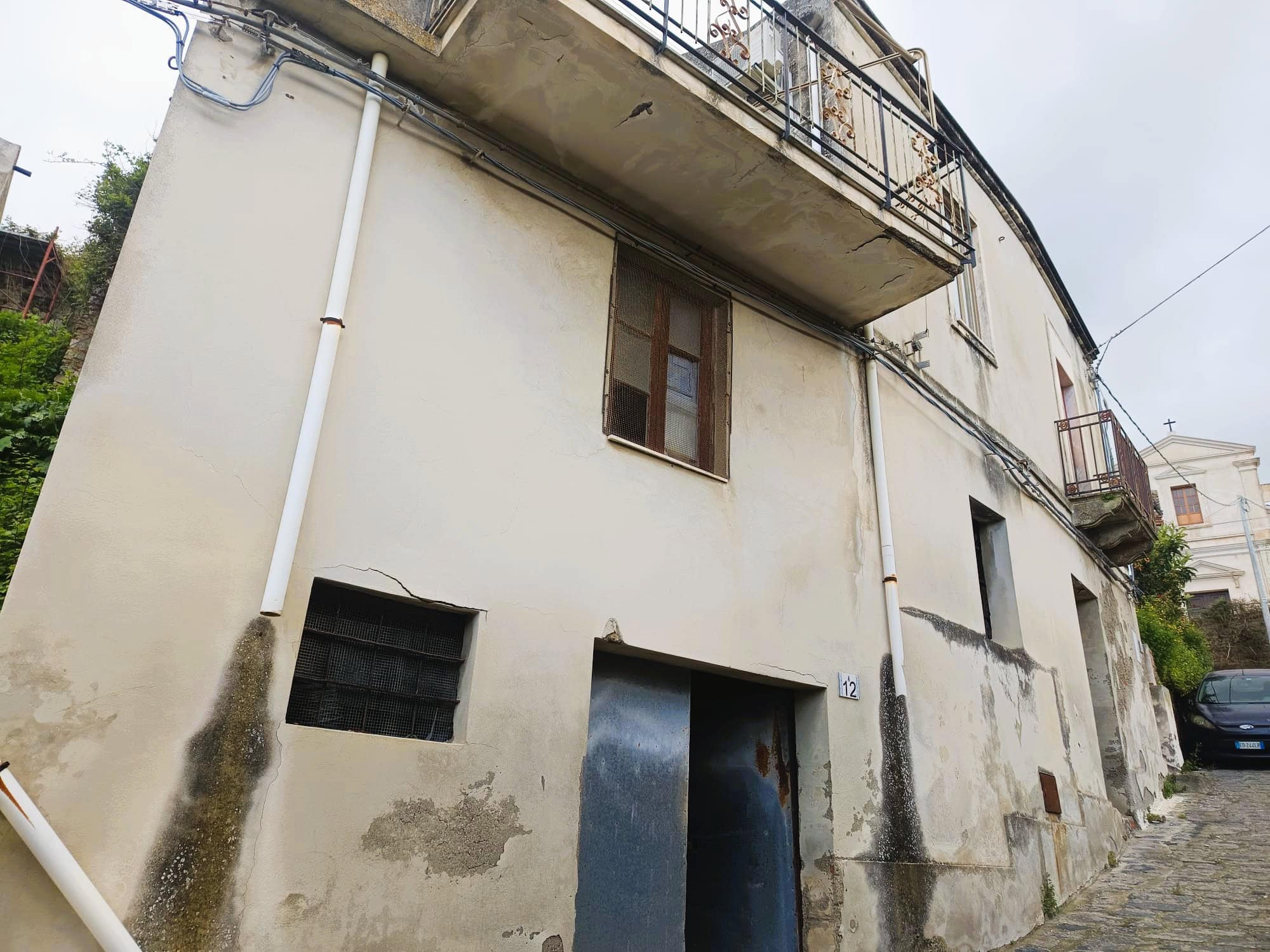 WhatsApp Image 2026-04-15 at 08.19.26 (2) Antico edificio residenziale in pietra con balcone e finestre in legno, situato in zona collinare con strada acciottolata e vista su case storiche.