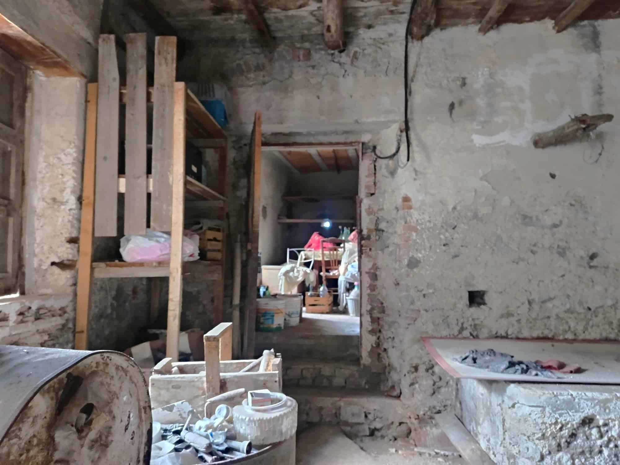 Interno di una casa in ristrutturazione con pareti in pietra, scaffali in legno e materiali da costruzione, pronta per lavori di rinnovamento e miglioramento abitativo.