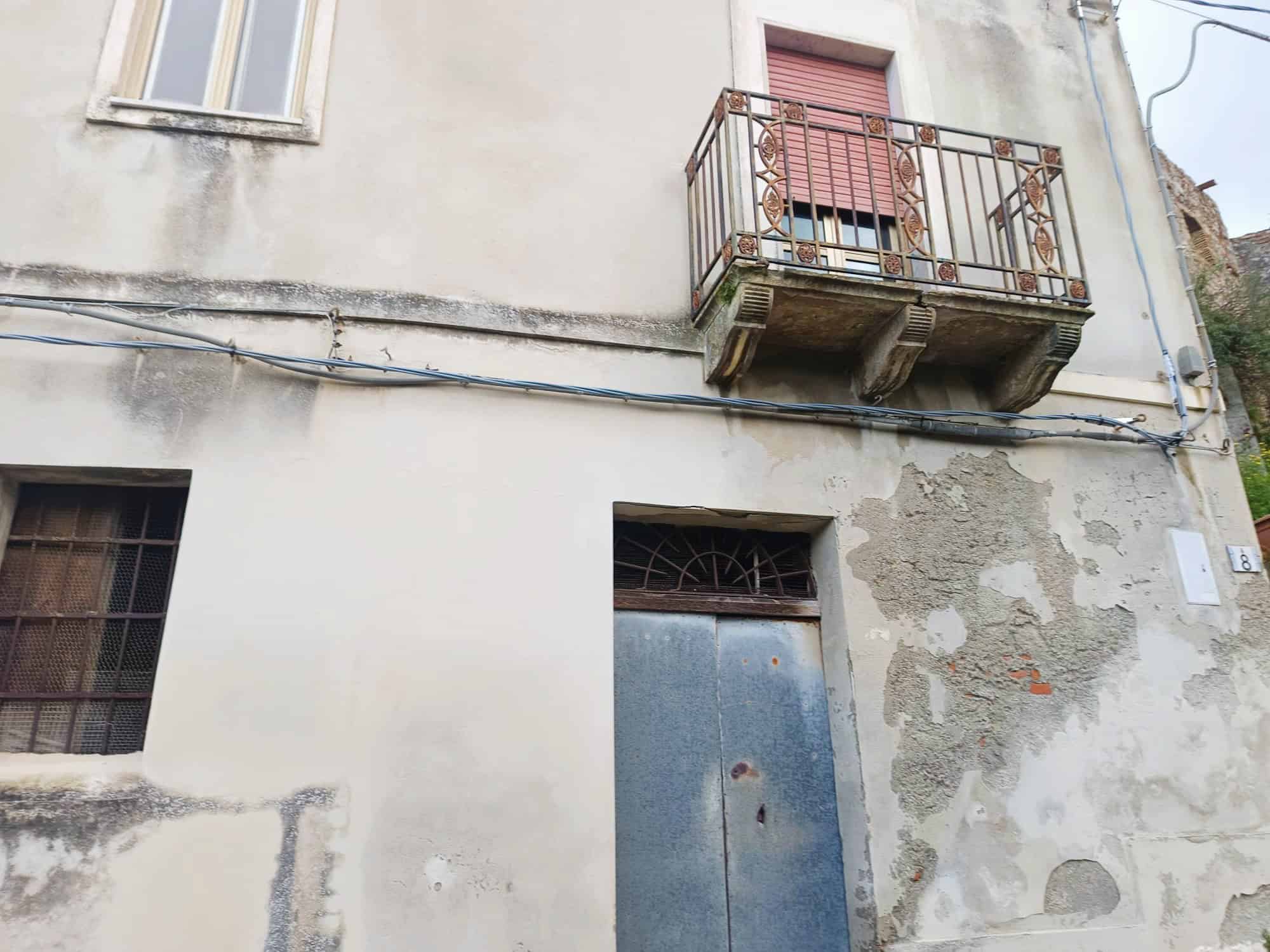 Vecchio edificio con balcone in ferro battuto e pareti in cattive condizioni, in un contesto urbano.