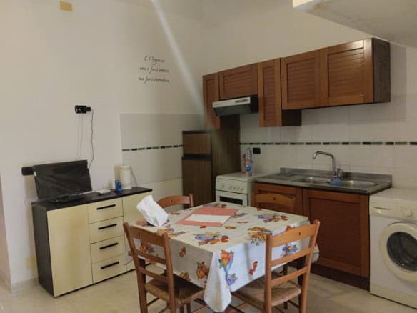 Lavatrice e cucina compatta in un appartamento arredato con mobili in legno e tavolo con tovaglia floreale, ideale per soggiorni brevi o studenti.