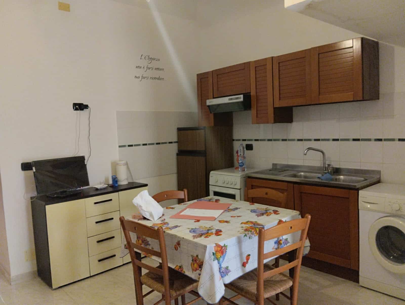 Lavatrice e cucina compatta in un appartamento arredato con mobili in legno e tavolo con tovaglia floreale, ideale per soggiorni brevi o studenti.