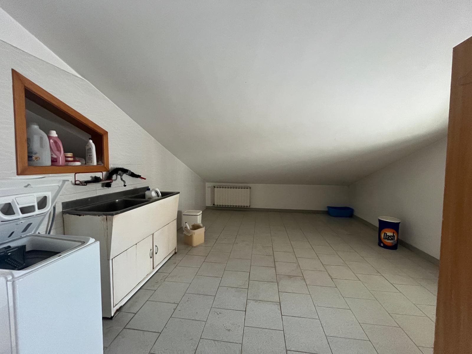 Lavanderia in soffitta con lavatrice, lavandino e spazio di stoccaggio, ambiente luminoso e spazioso ideale per le faccende domestiche.