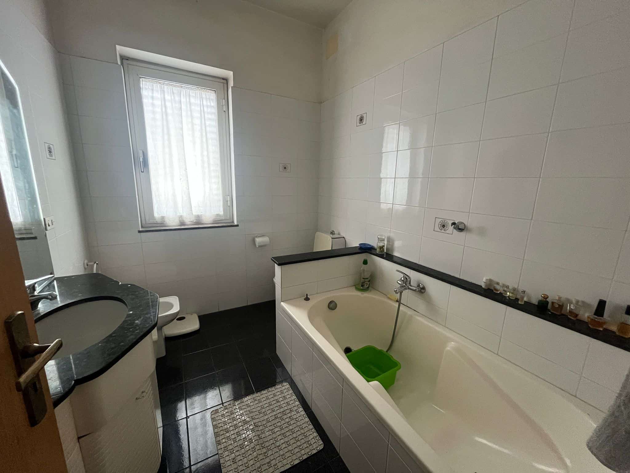 Lavabo e vasca da bagno in un bagno spazioso con finestra, piastrelle bianche e dettagli neri, ideale per ristrutturazioni e miglioramenti domestici.