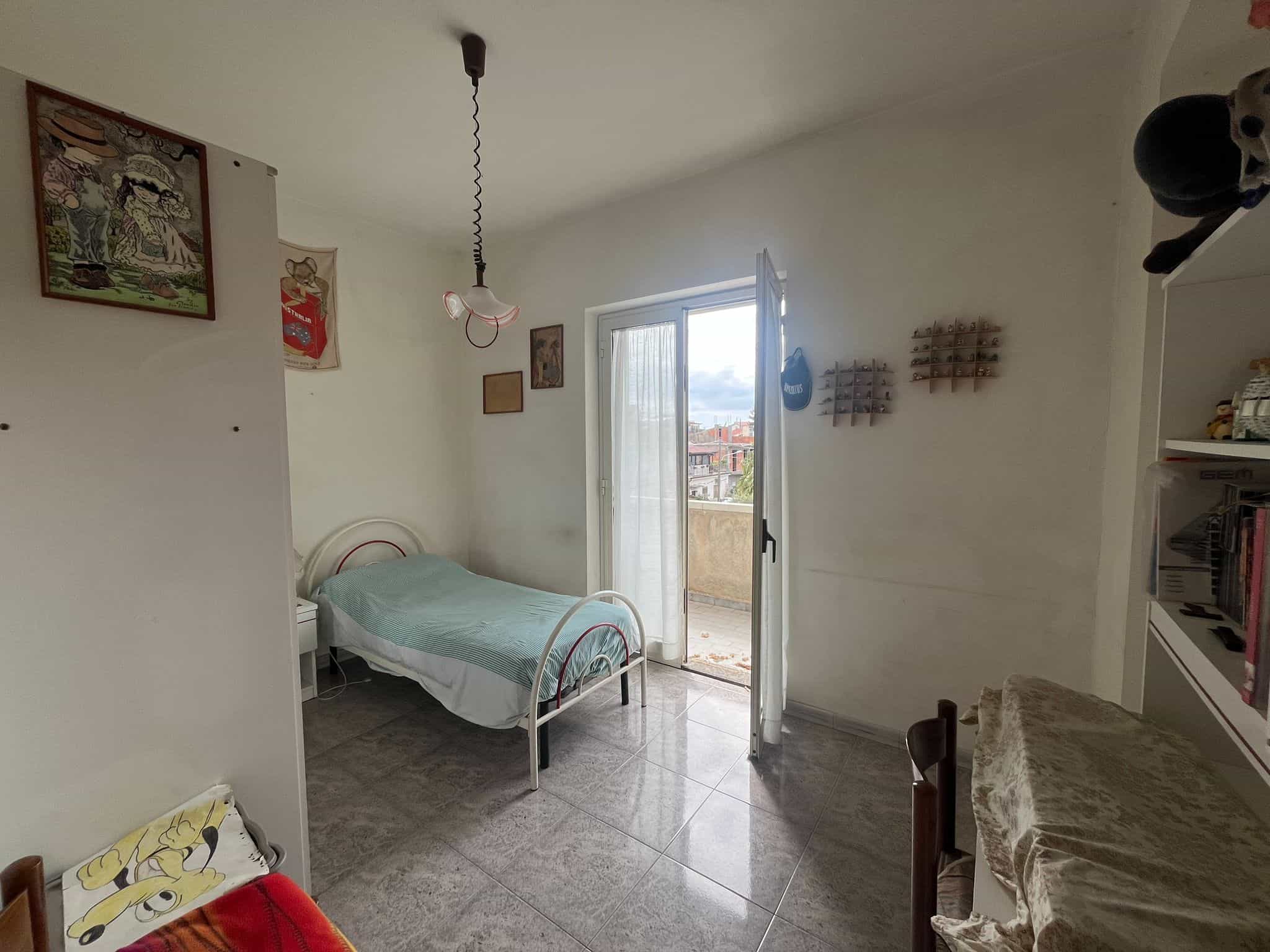 Camera da letto luminosa con balcone, arredi semplici e pareti decorate, ideale per soggiorno confortevole in zona residenziale tranquilla.
