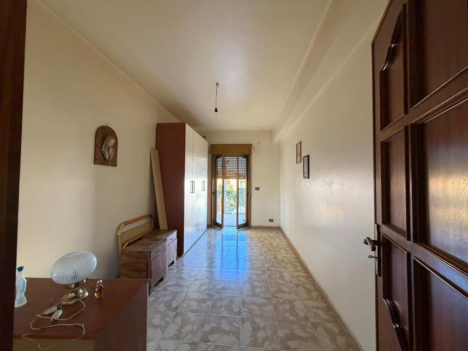 Interno di un appartamento con pareti bianche, mobili in legno e porta finestra che dà su un balcone, ideale per chi cerca soluzioni abitative a NextCasa.