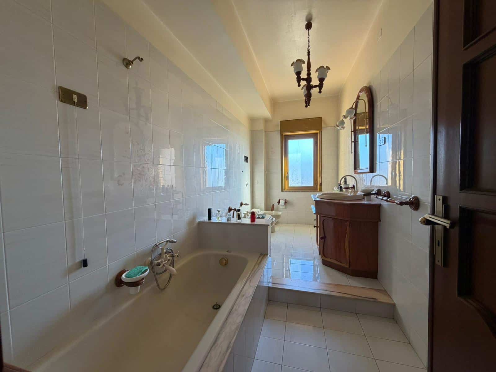 Il bagno spazioso con vasca e lavabo in legno, illuminato dalla luce naturale proveniente dalla finestra, presenta un design classico e funzionale, ideale per il comfort quotidiano.