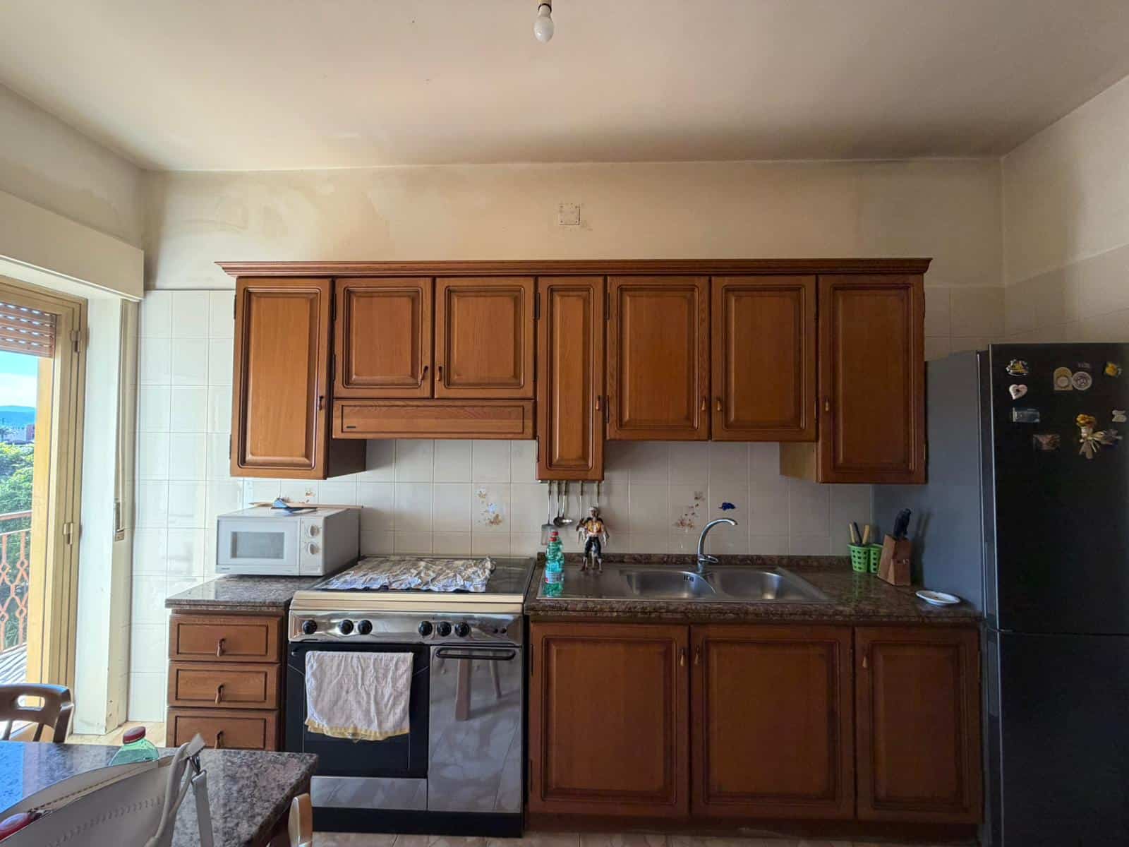 Pannello di cucina in legno con elettrodomestici moderni, forno, frigorifero e lavello, in un ambiente domestico luminoso e accogliente, ideale per cucinare e vivere quotidianamente.