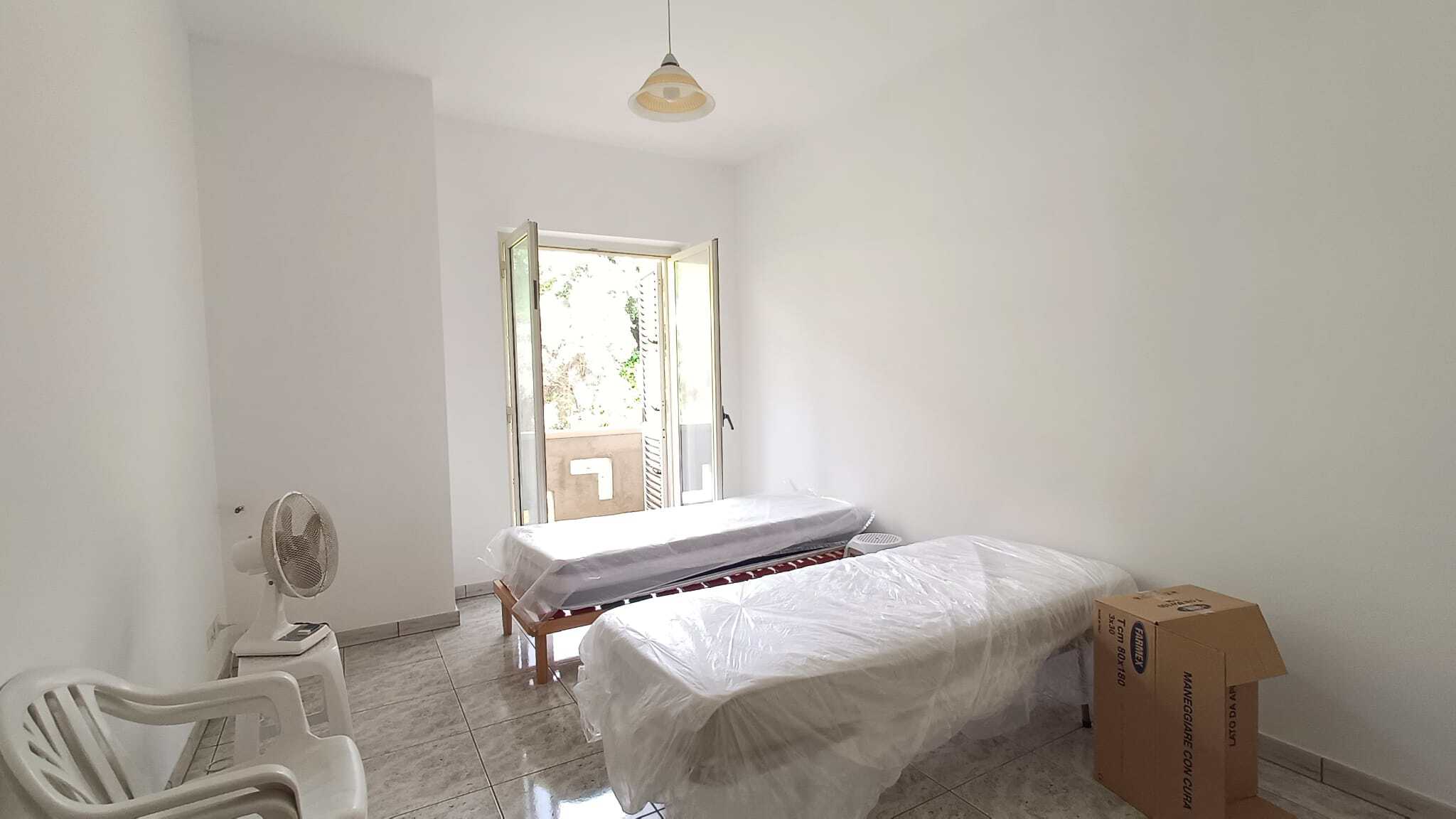 Letto singolo e letto matrimoniale in una stanza luminosa con pareti bianche e finestra aperta, pronta per l'arredamento.