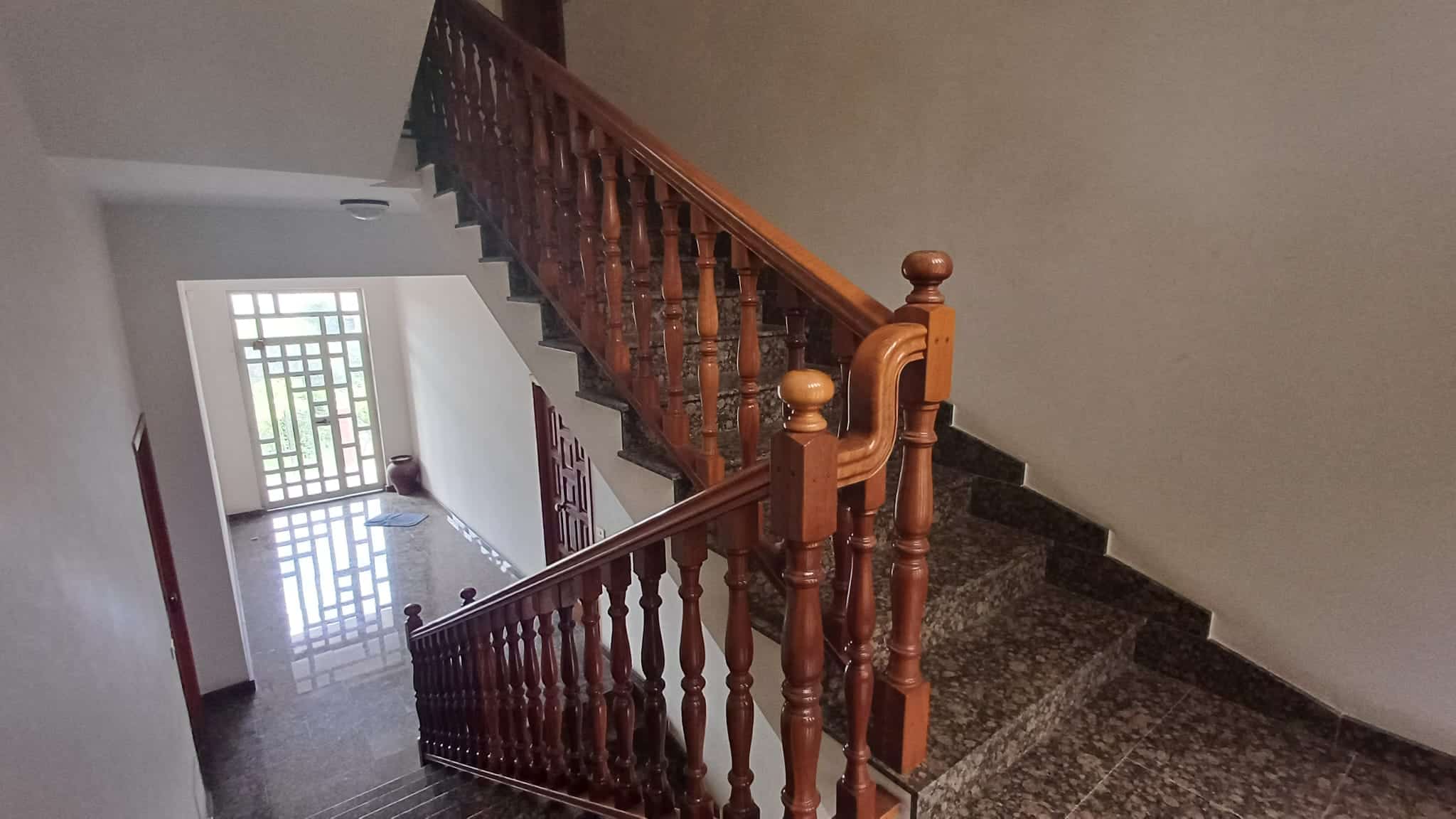 Elegante scala in legno con ringhiera decorativa in un ingresso di casa moderna, illuminata da luce naturale, ideale per interni di proprietà residenziali di alta qualità.
