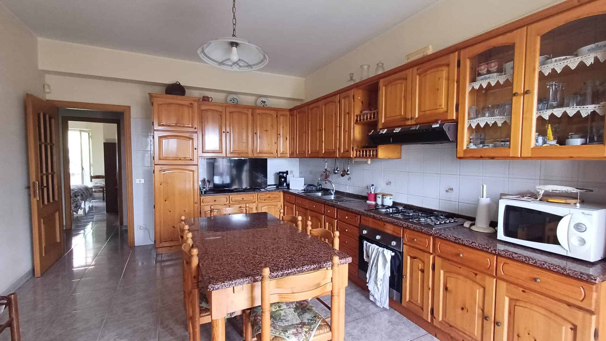 Piano cucina in legno con piano di lavoro in granito, elettrodomestici moderni e spazio per la colazione, in un ambiente luminoso e accogliente.
