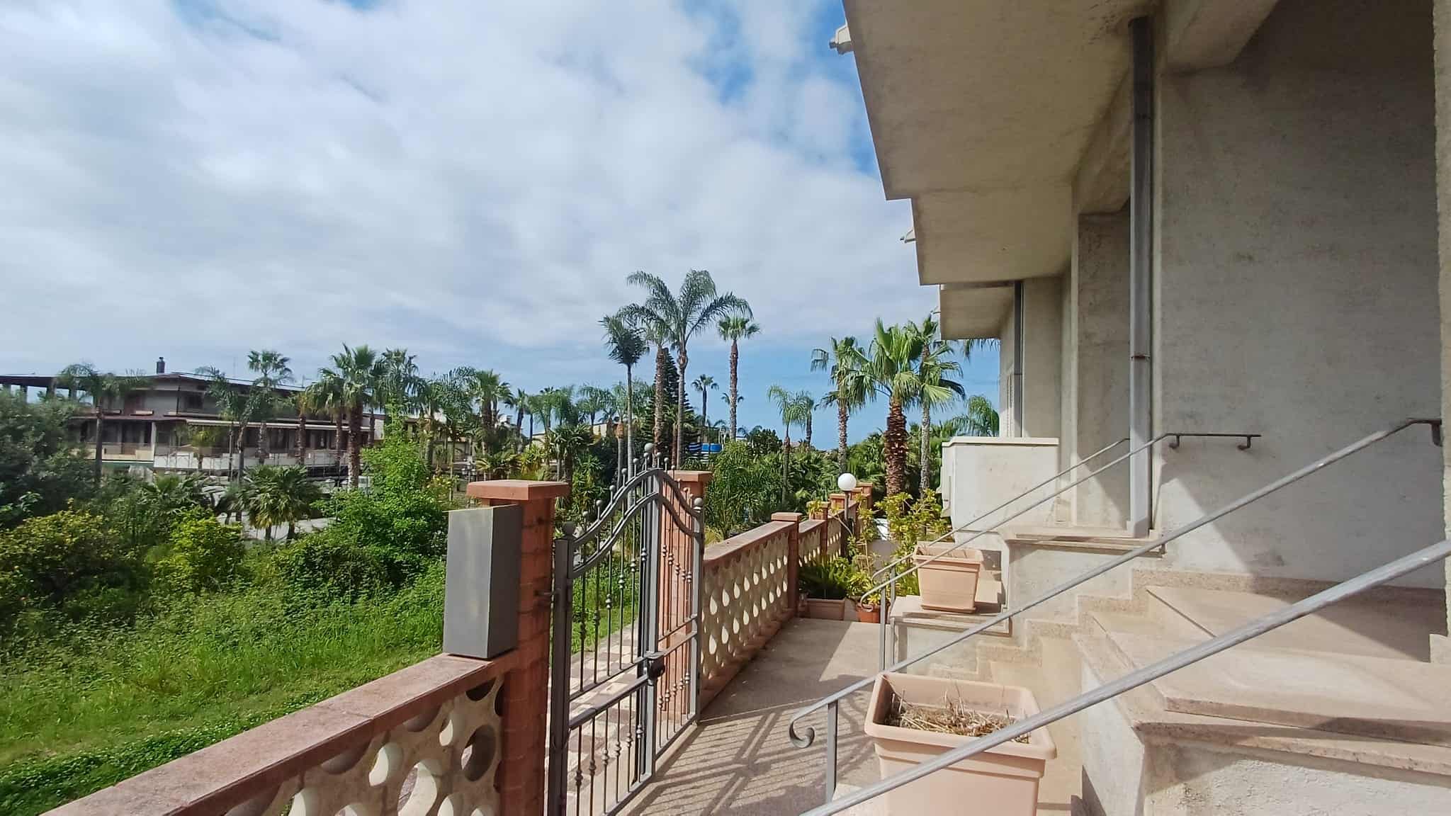 Ampia terrazza con vista su giardino tropicale e palme, ideale per relax e convivialità, con accesso diretto alle zone living di un appartamento di lusso a NextCasa.