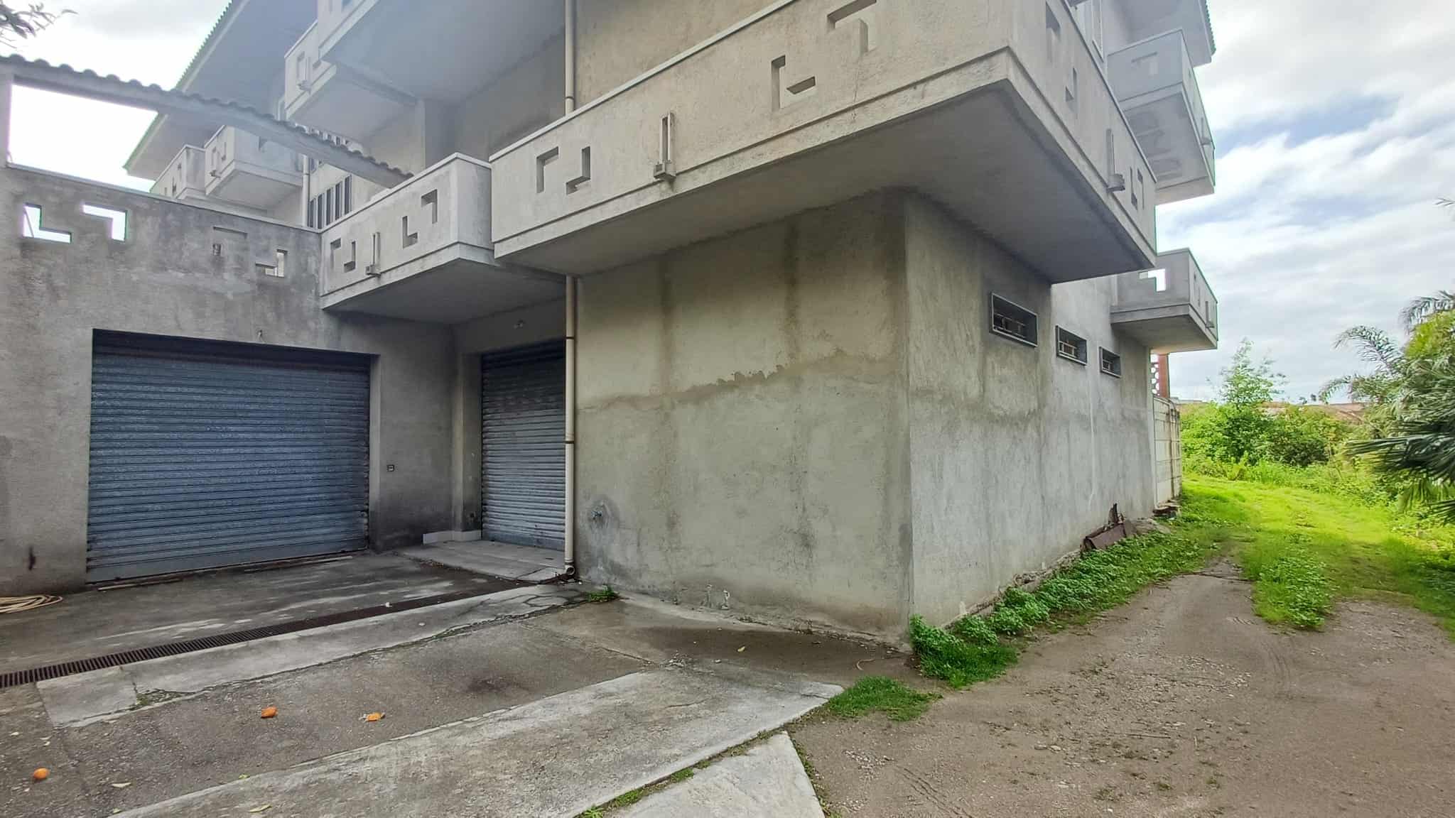 Porte garage in metallo e struttura in cemento di un edificio residenziale in fase di costruzione, con area di parcheggio e spazio verde circostante.