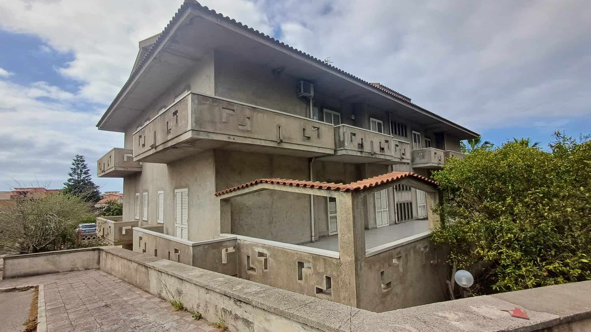 Ampia casa residenziale in stile moderno con balconi e terrazze, situata in un'area tranquilla circondata da vegetazione, ideale per famiglie e investitori immobiliari.