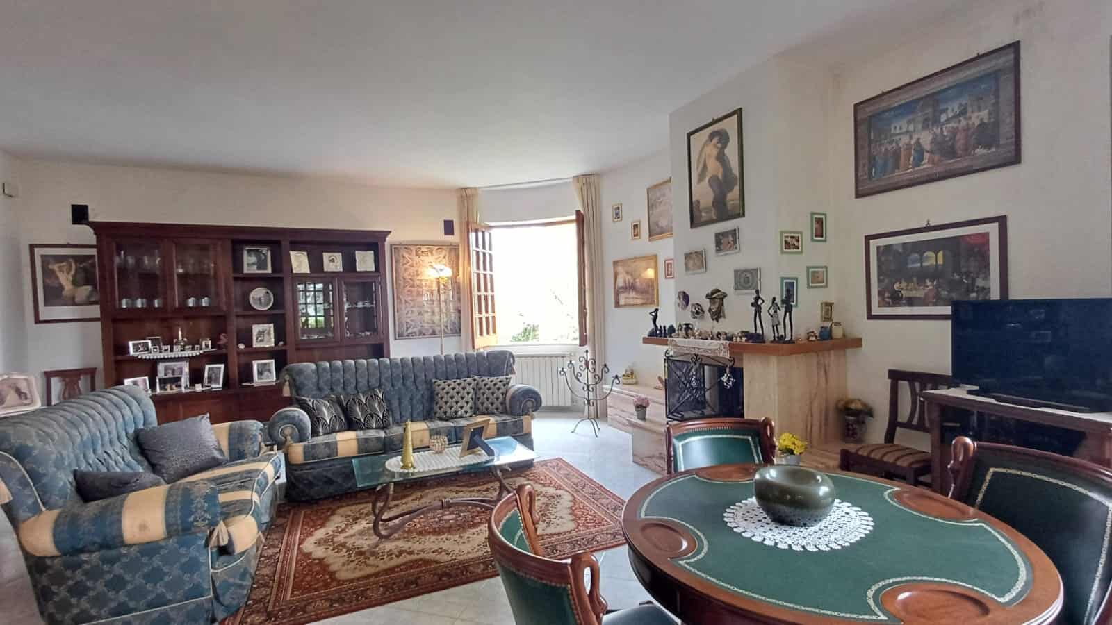 Elegante soggiorno con divani blu e arredi classici, decorato con quadri e oggetti d'arte, illuminato da luce naturale, ideale per vivere momenti di relax e convivialità.