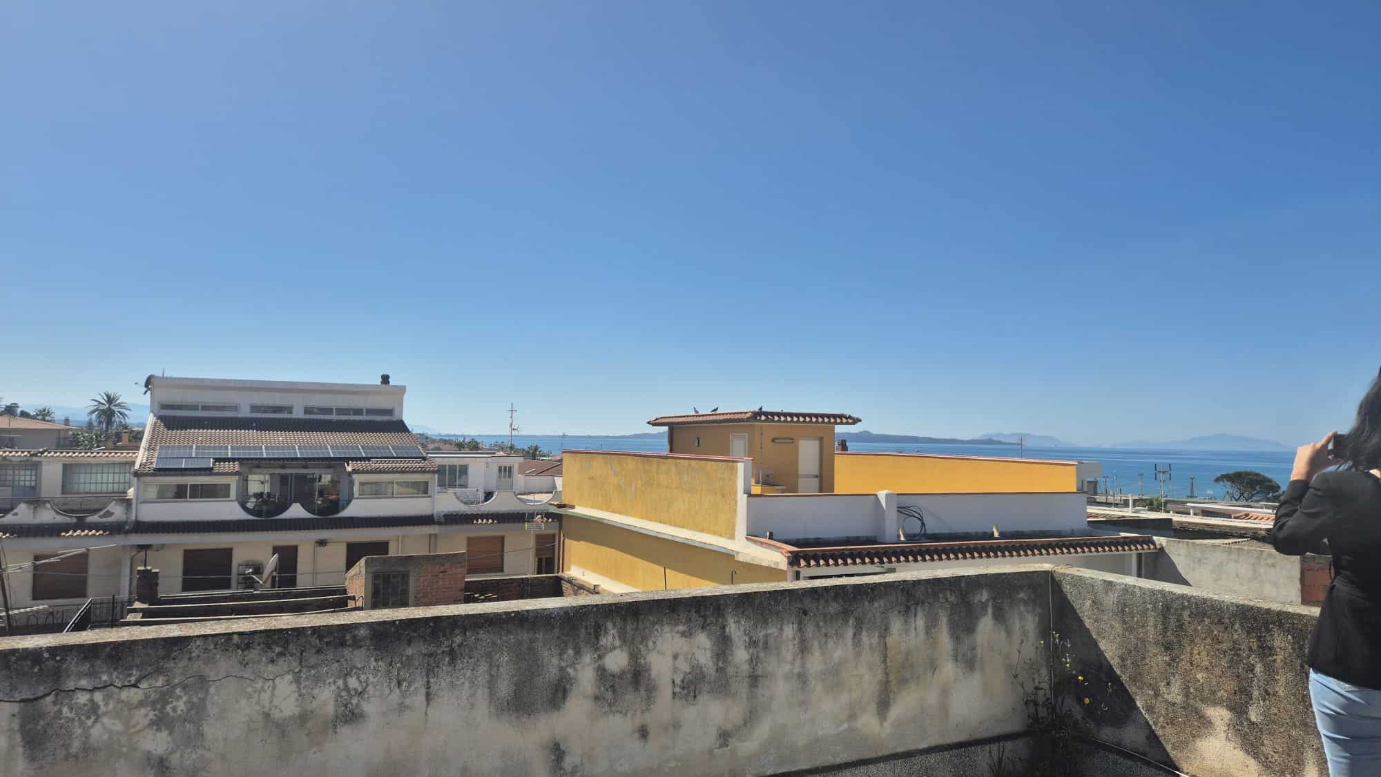 Vista panoramica di un quartiere residenziale con edifici moderni e il mare sullo sfondo, sotto un cielo sereno e azzurro.