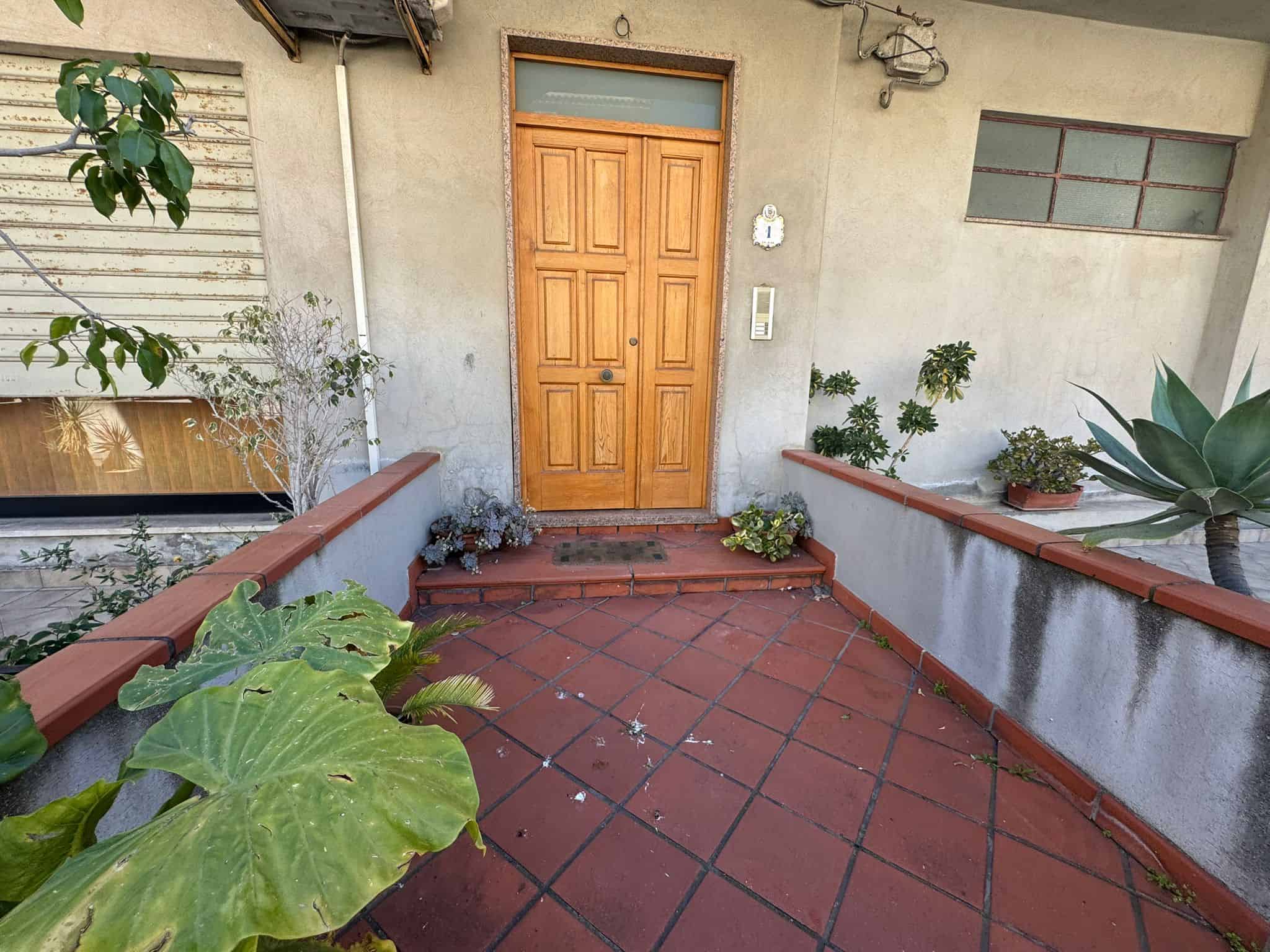 Porte d'ingresso in legno naturale con accessori moderni, ingresso accogliente e ben curato con piante ornamentali e decorazioni, ideale per valorizzare l'entrata di una casa in stile rustico o contem.