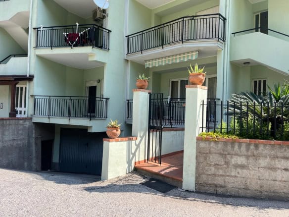 Balcone di un appartamento con ringhiera in metallo nero, piante in vaso e accesso tramite scala, edificio residenziale moderno con pareti verdi e balconi sovrapposti.