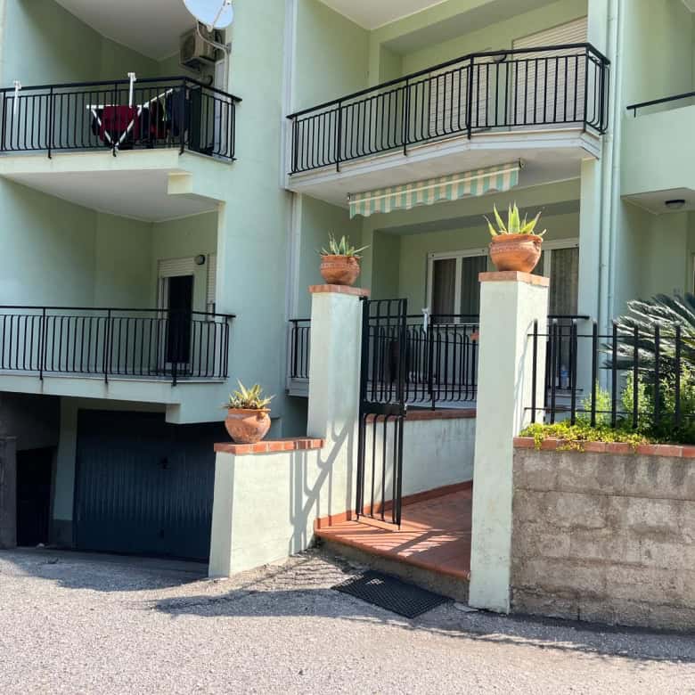 Balcone di un appartamento con ringhiera in metallo nero, piante in vaso e accesso tramite scala, edificio residenziale moderno con pareti verdi e balconi sovrapposti.