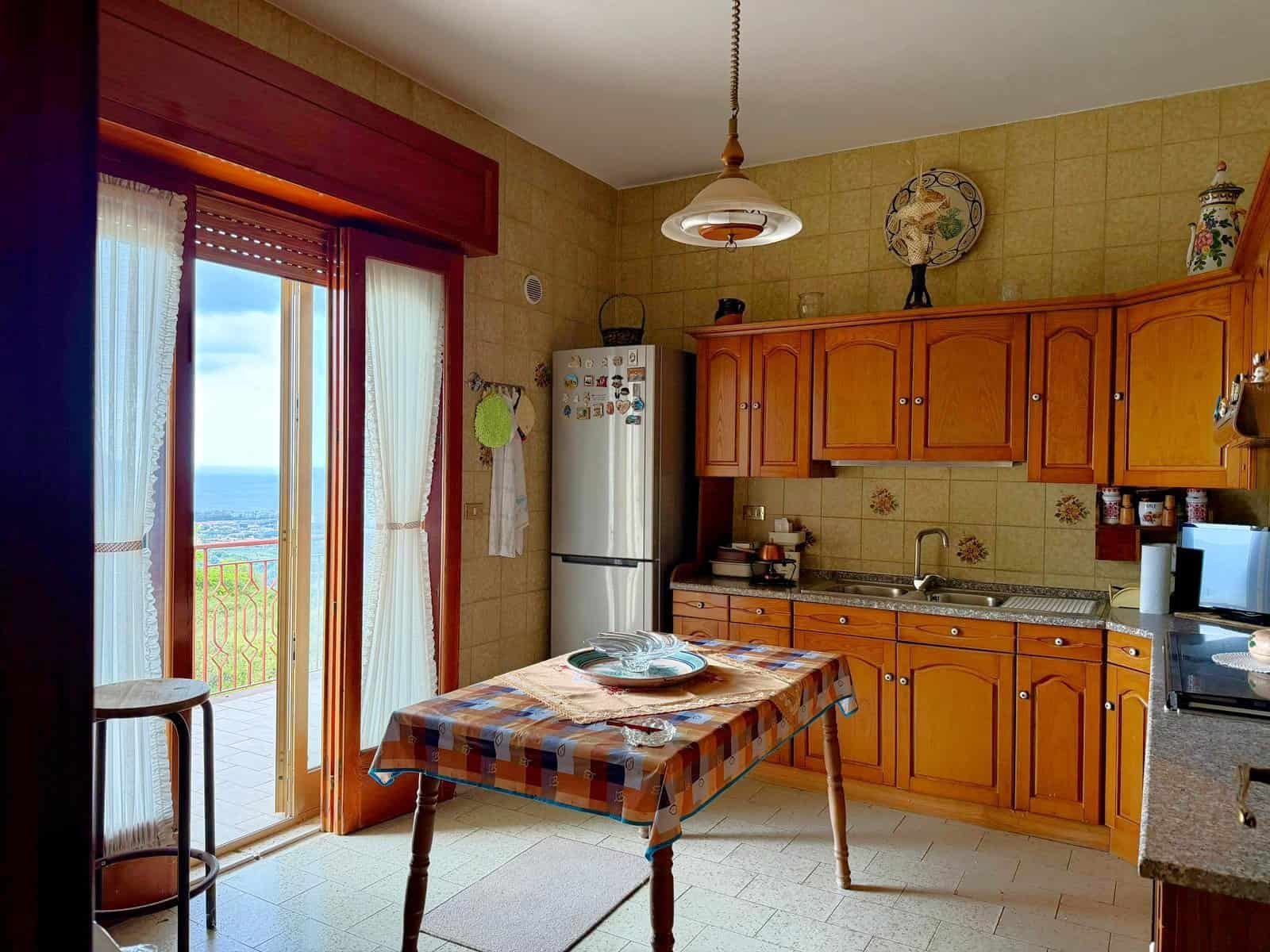 Pannello di cucina con mobili in legno, frigorifero e accessori, vista su balcone con vista panoramica sul mare, ambiente accogliente e luminoso, ideale per vivere momenti di relax e convivialità.