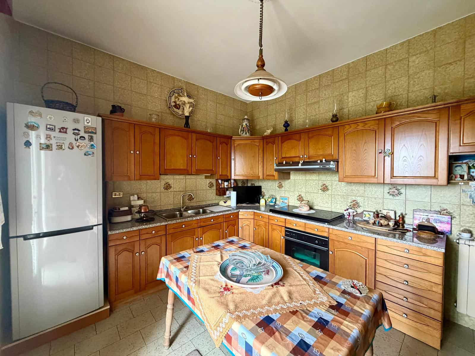 Cucina abitabile con mobili in legno, frigorifero, piano cottura e tavolo da pranzo, ambiente accogliente e funzionale in stile tradizionale italiano.