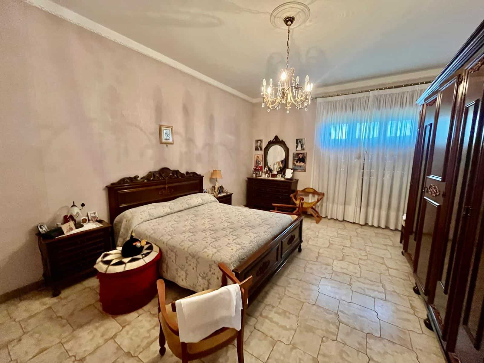 Elegante camera da letto con arredi classici, grande armadio in legno, letto matrimoniale e lampadario chandelier, ambiente luminoso e accogliente, ideale per vivere momenti di relax e comfort.