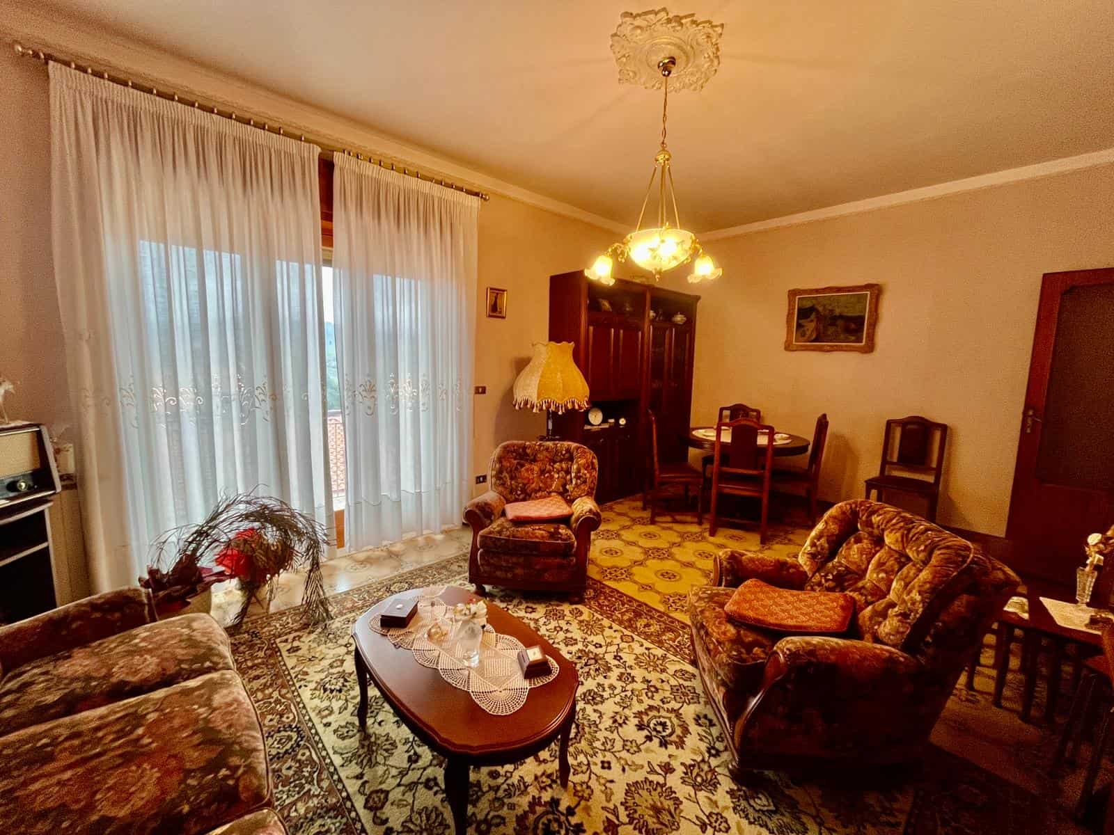 Appartamento classico con soggiorno arredato con divani e poltrone in stile vintage, illuminato da lampadari e decorazioni d'epoca, con grandi finestre che lasciano entrare molta luce naturale.