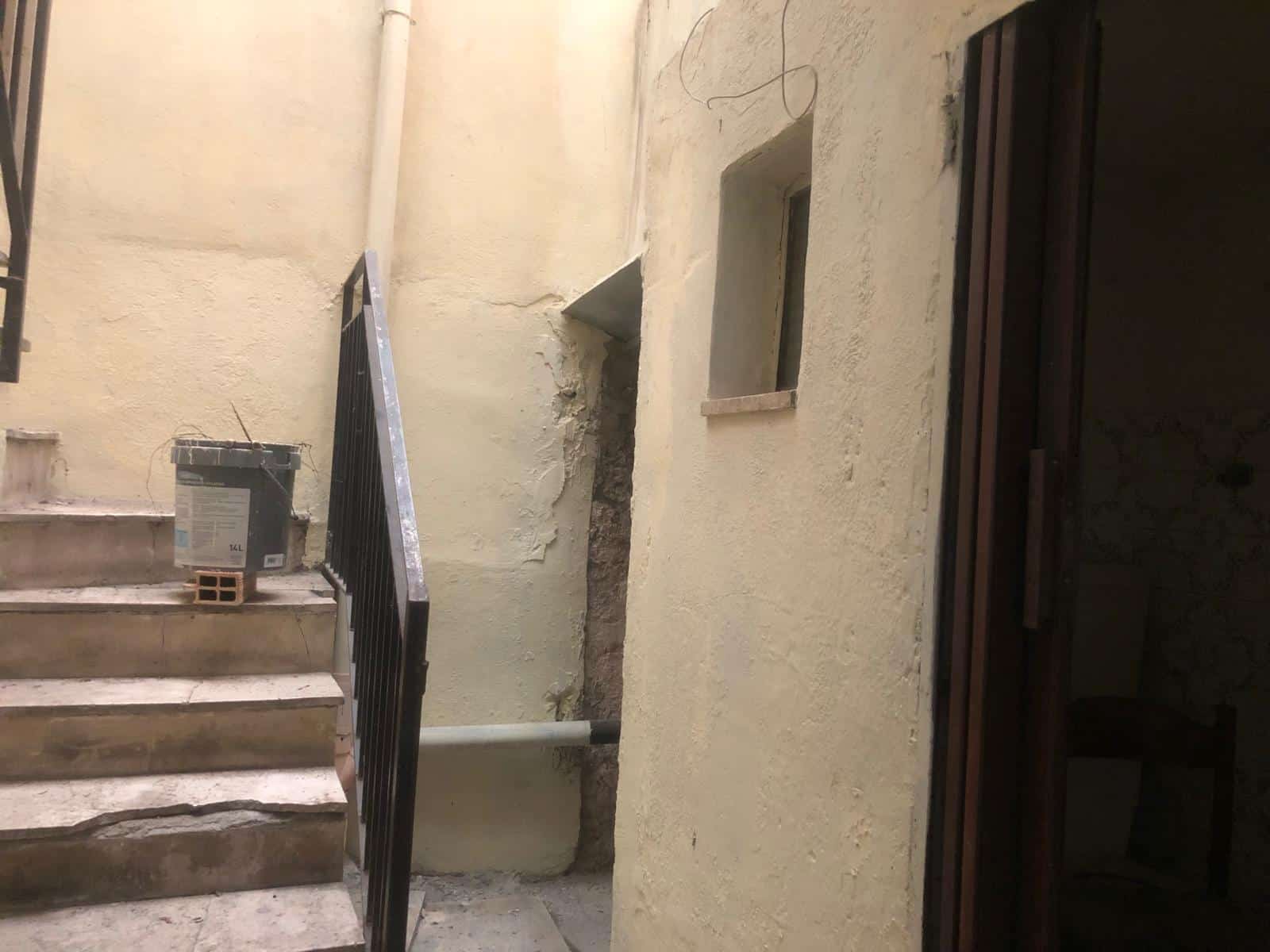 Porte di accesso a un cortile interno di un edificio storico con pareti in pietra e scale in pietra, caratterizzato da un ambiente rustico e autentico.