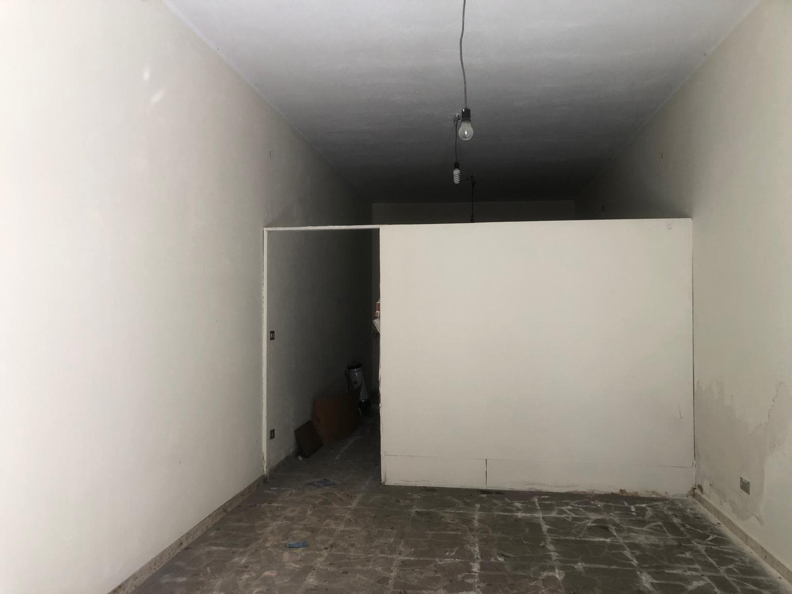 Interno di un appartamento in fase di ristrutturazione con pareti bianche e pavimento in cemento, pronto per essere arredato.