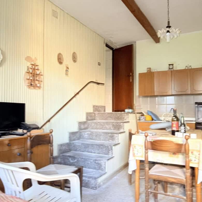 Ampia zona soggiorno con cucina aperta, tavolo da pranzo e scala in pietra che collega ai piani superiori, arredamento accogliente e dettagli decorativi tradizionali, ambiente luminoso e funzionale.