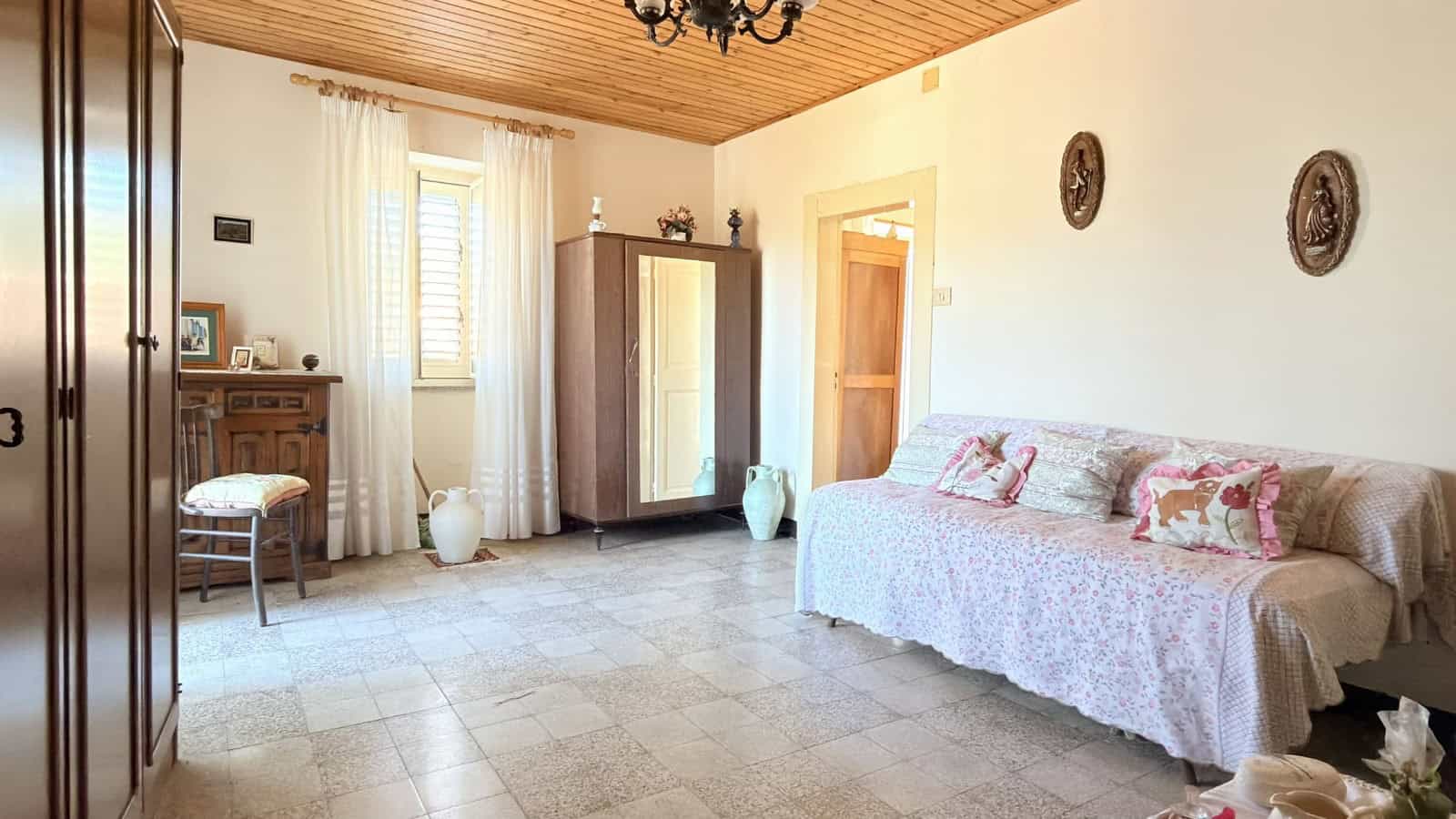 Poltrona e armadio in soggiorno con pareti chiare e decorazioni vintage, ambiente luminoso e accogliente.