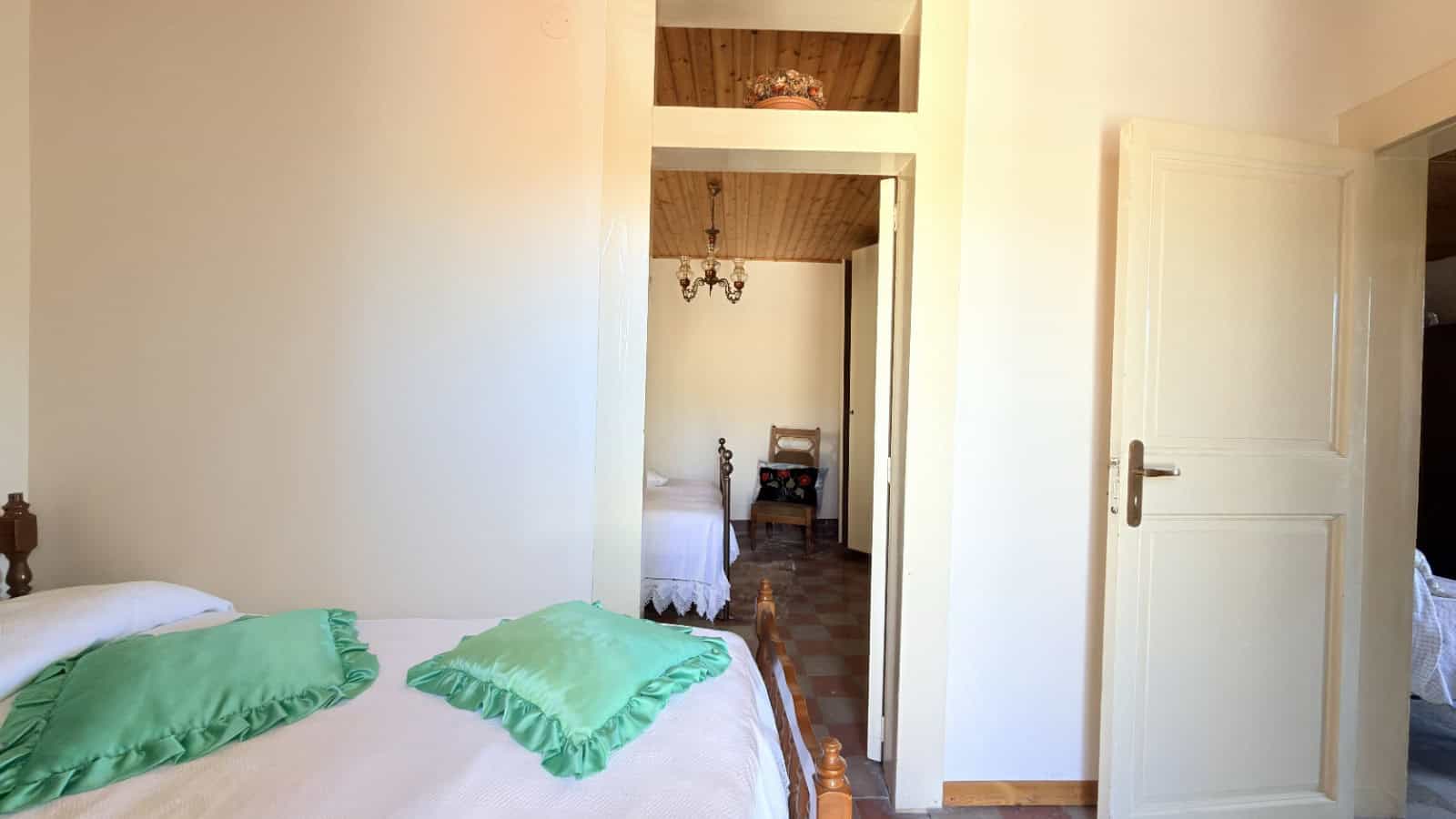 Letto matrimoniale con cuscini verdi in una camera da letto luminosa e accogliente, con porta aperta che rivela un'altra stanza arredata con mobili classici. Ideale per case in vendita o affitto, con.