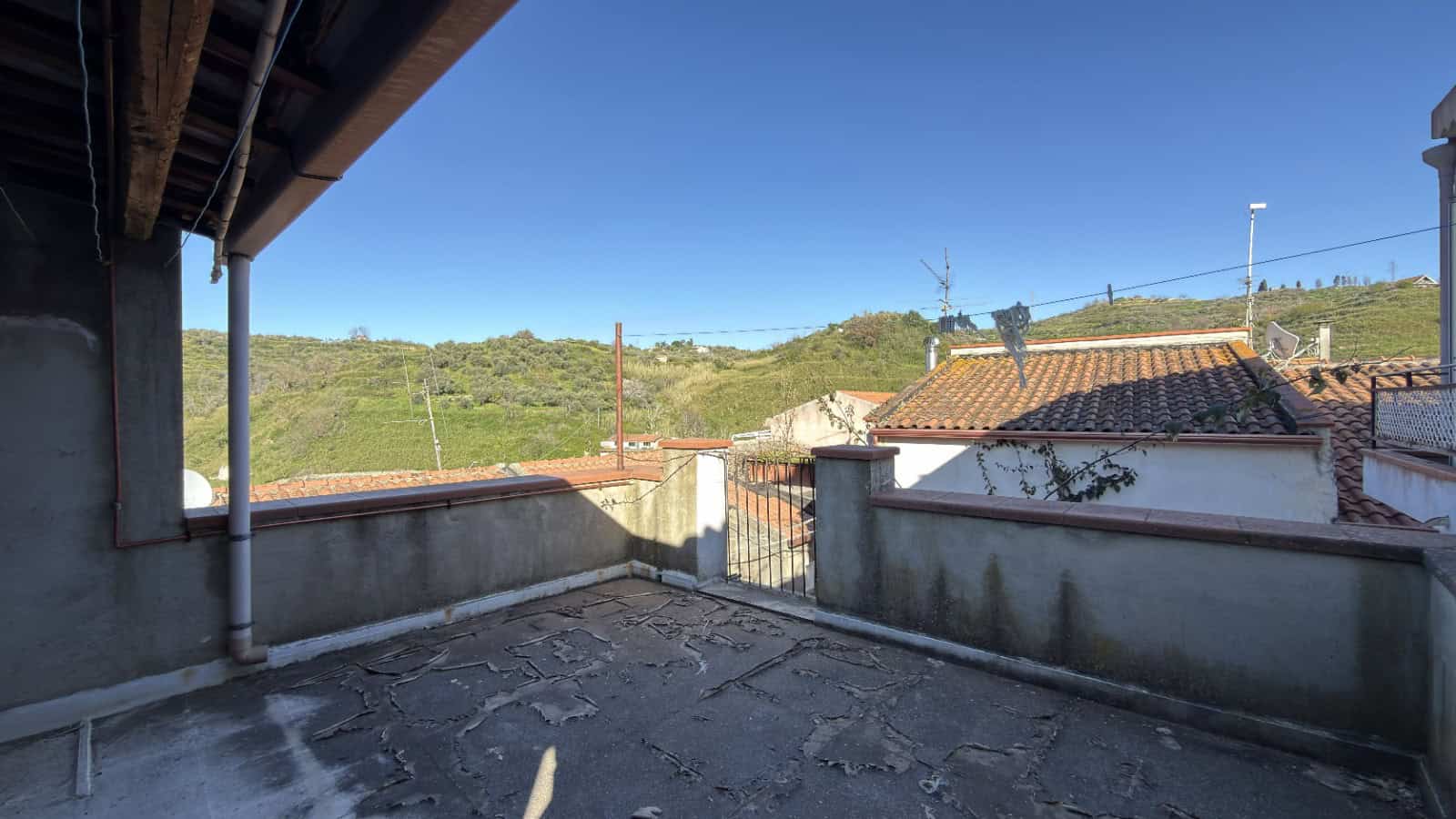 Balcone con vista panoramica su colline verdi e case tradizionali italiane, in un ambiente residenziale tranquillo e soleggiato, ideale per relax e momenti all'aperto.