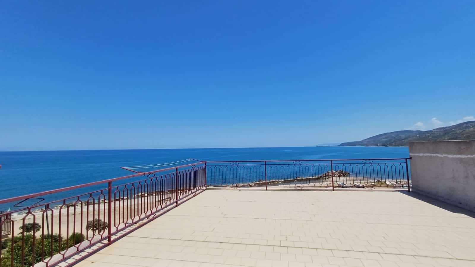 Vista panoramica sul mare dal terrazzo di una casa in Italia, con ringhiera in ferro battuto e paesaggio costiero sullo sfondo, ideale per immobili di lusso e proprietà fronte mare.