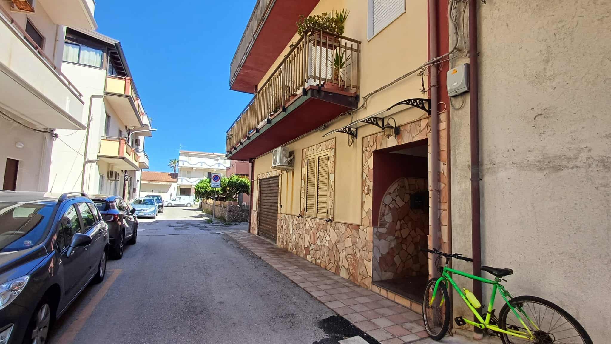 Pannello solare installato sul tetto di un edificio residenziale in un quartiere urbano soleggiato, con auto parcheggiate lungo la strada.