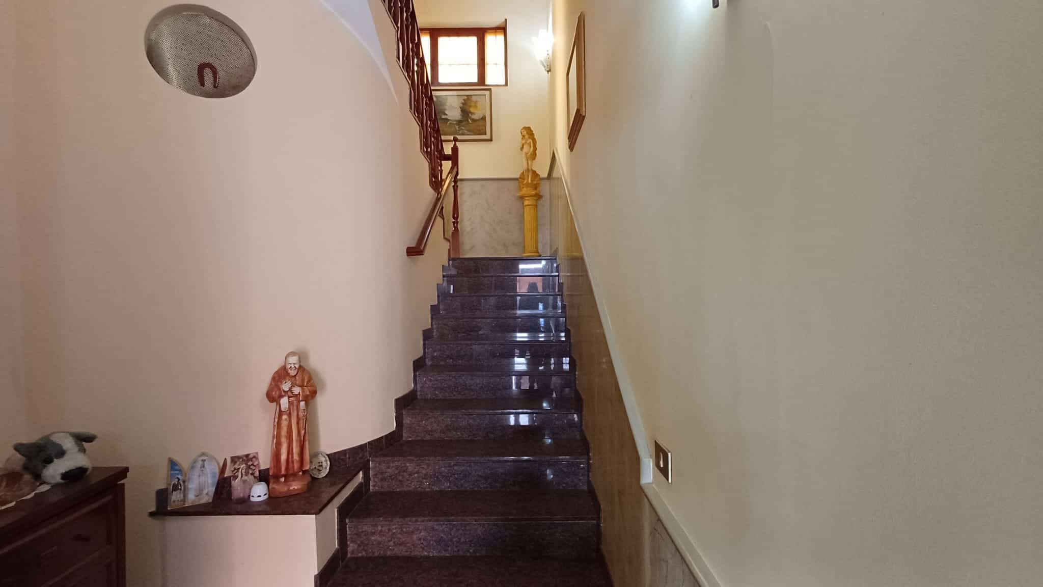 Escalier interno in marmo con ringhiera in legno, ingresso elegante di una casa moderna, dettagli decorativi e luce naturale che illumina l'ambiente.