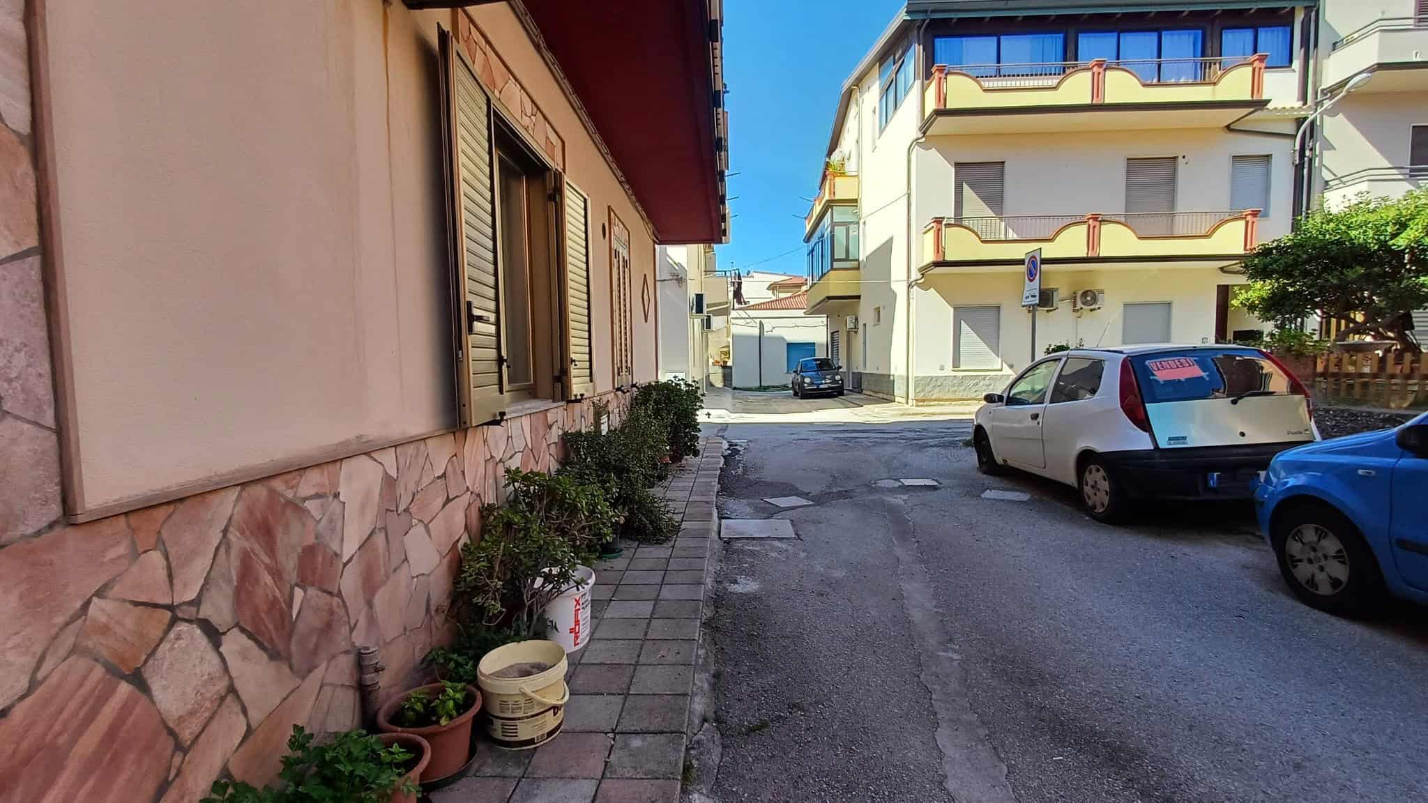 Ampia strada urbana con edifici residenziali, auto parcheggiate e piante ornamentali, rappresentativa di un quartiere tranquillo e ben curato in Italia.
