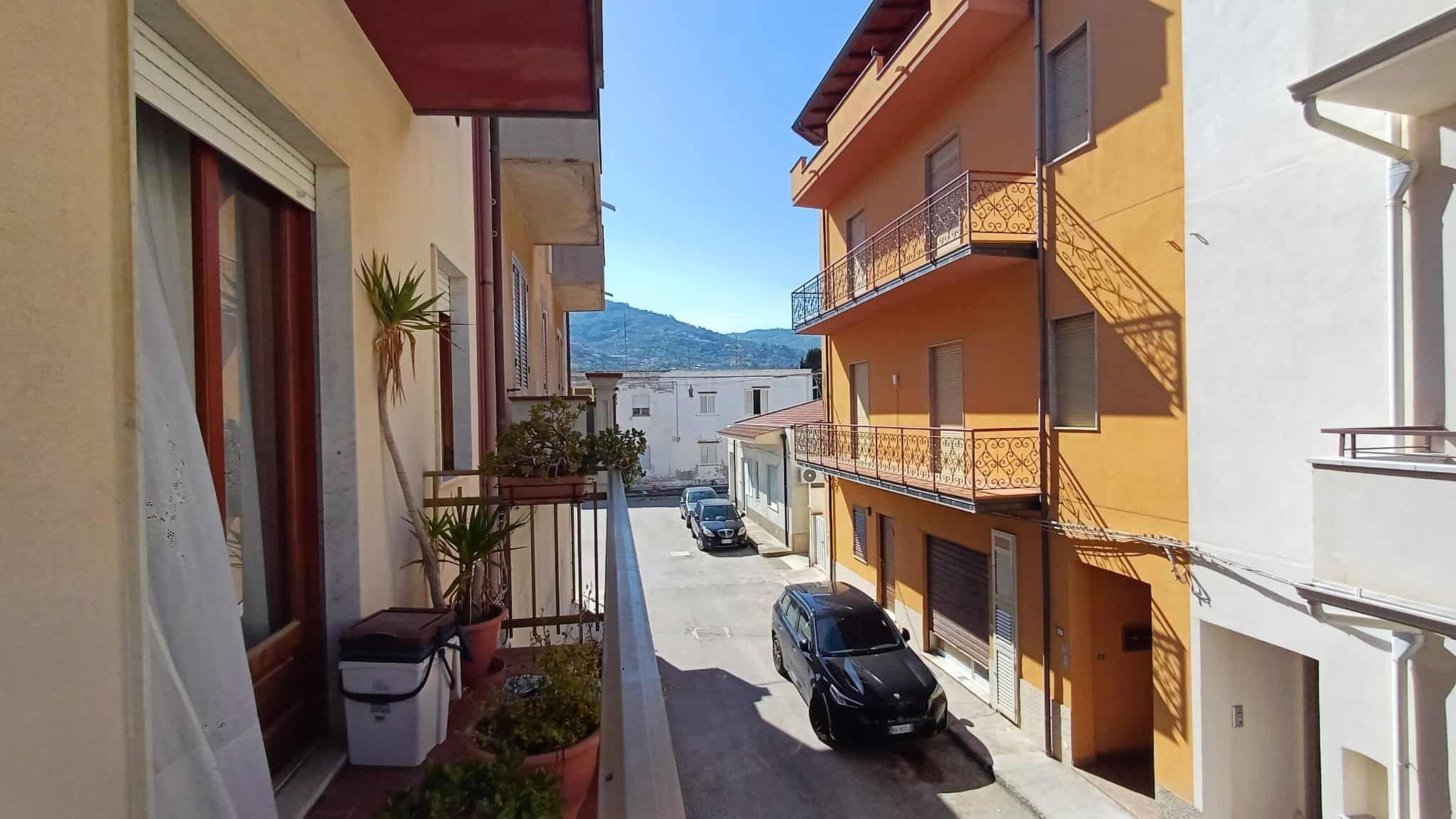 Vista di un vicolo urbano con edifici residenziali colorati, auto parcheggiate e un cielo sereno, rappresentando un tipico scenario di quartiere in Italia.